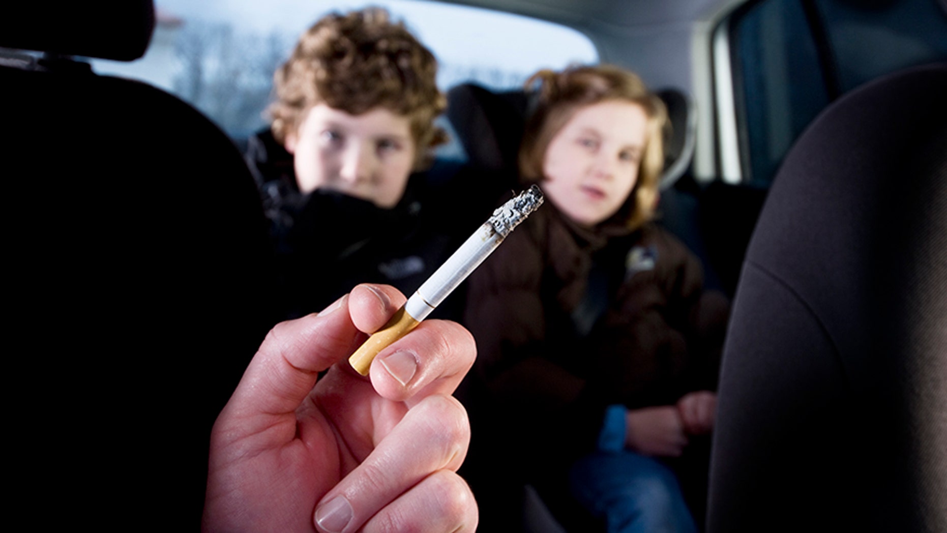 Two young children being subjected to the effects of passive smoking from their mother's cigarette.