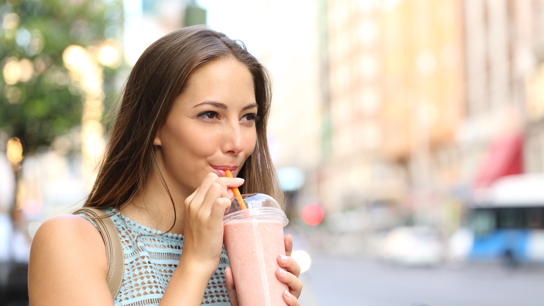 Pensive happy woman sipping a milkshake in the street
