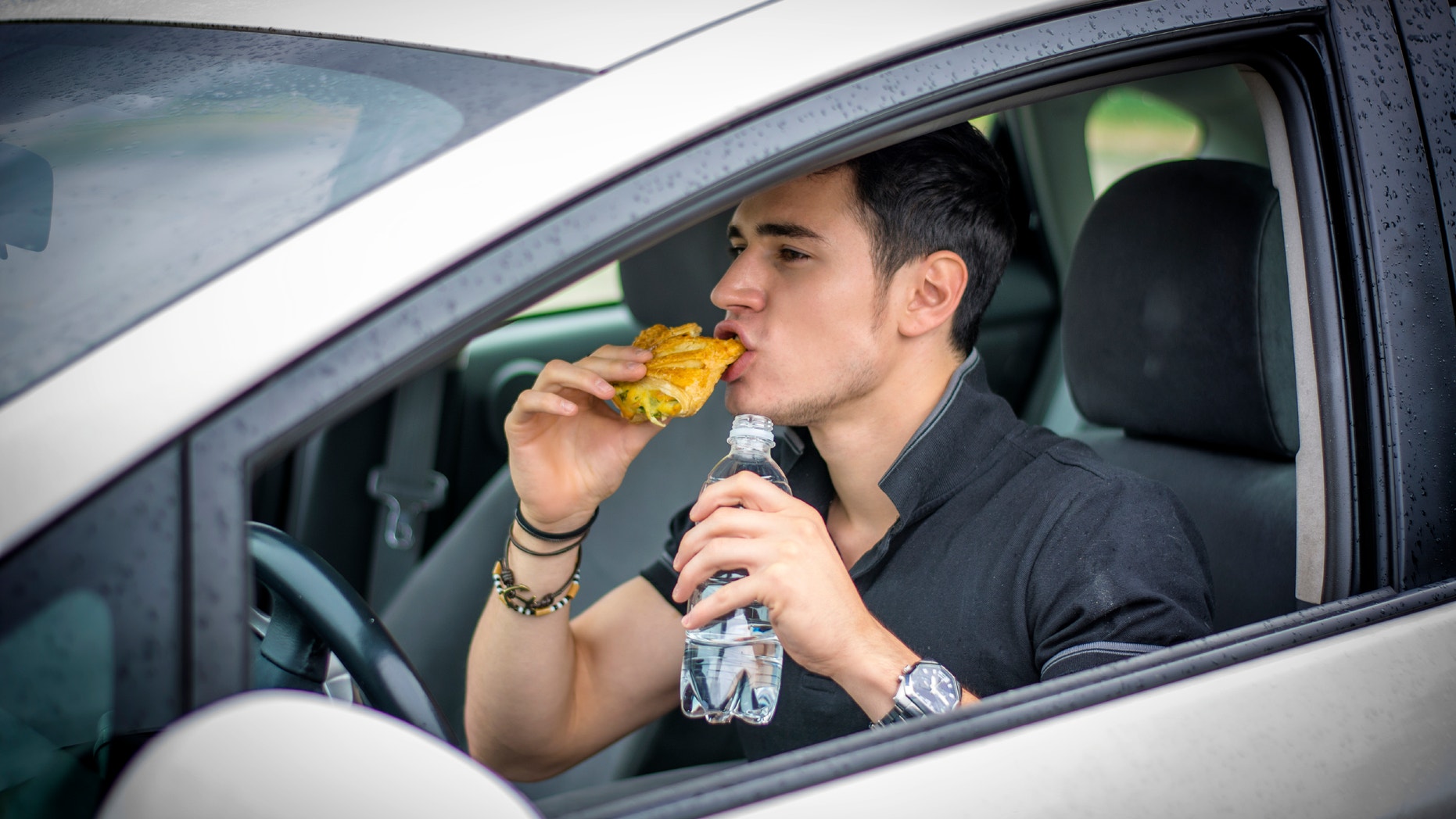 Young handsome man driving his car while eating food in the traffic