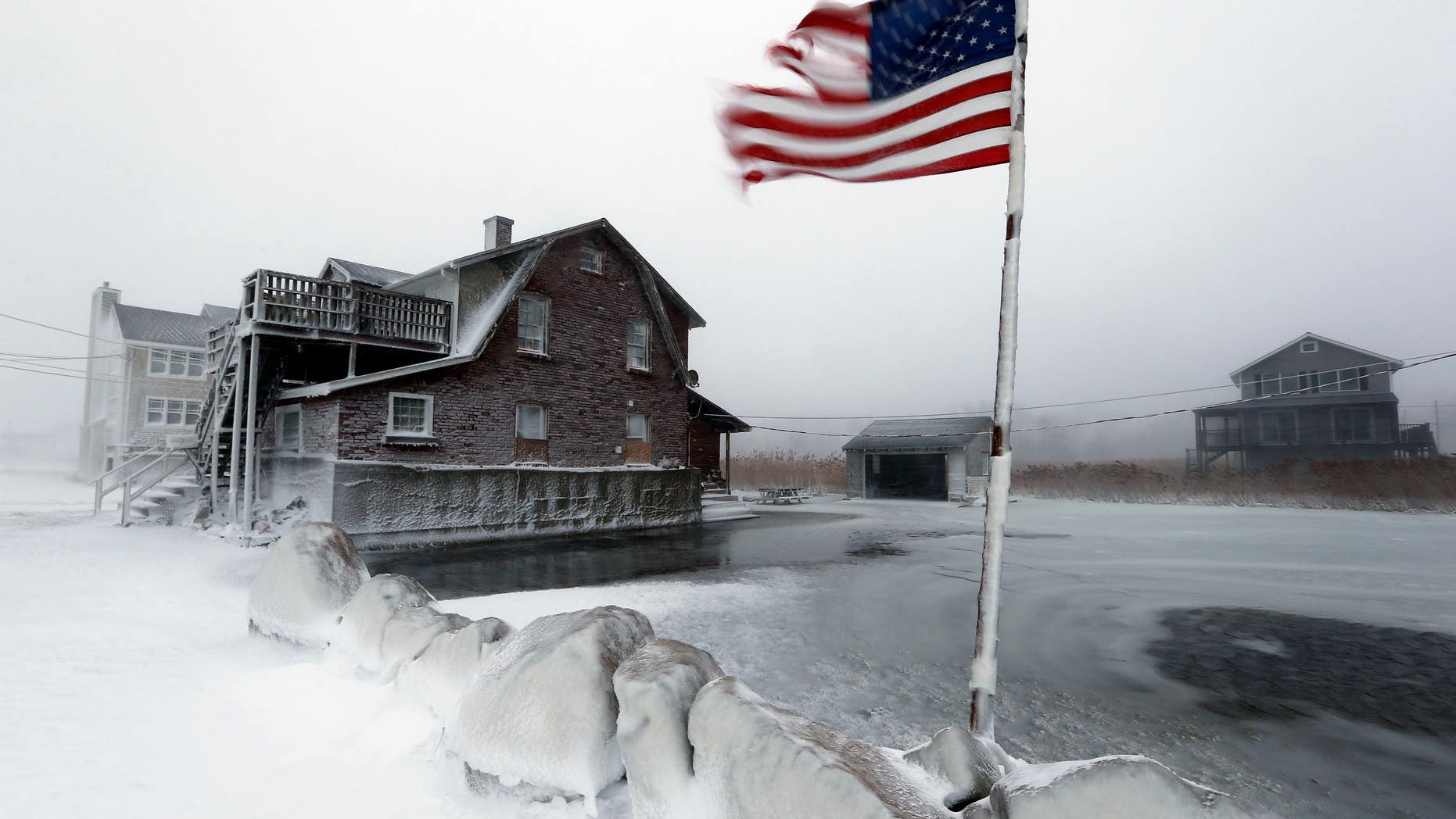 A tattered flag flies by a flooded yard along the shore in Scituate, Mass., Friday, Jan. 3, 2014. A blustering winter storm that dropped nearly 2 feet of snow just north of Boston, shut down major highways in New York and Pennsylvania and forced U.S. airlines to cancel thousands of flights nationwide menaced the Northeast on Friday with howling winds and frigid temperatures. (AP Photo/Michael Dwyer)