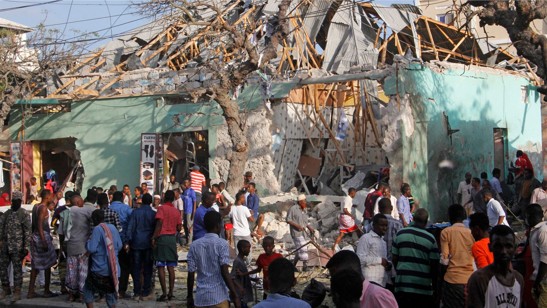 Somalis stand outside a destroyed building after a car bomb in Mogadishu, Somalia Thursday, March 22, 2018.