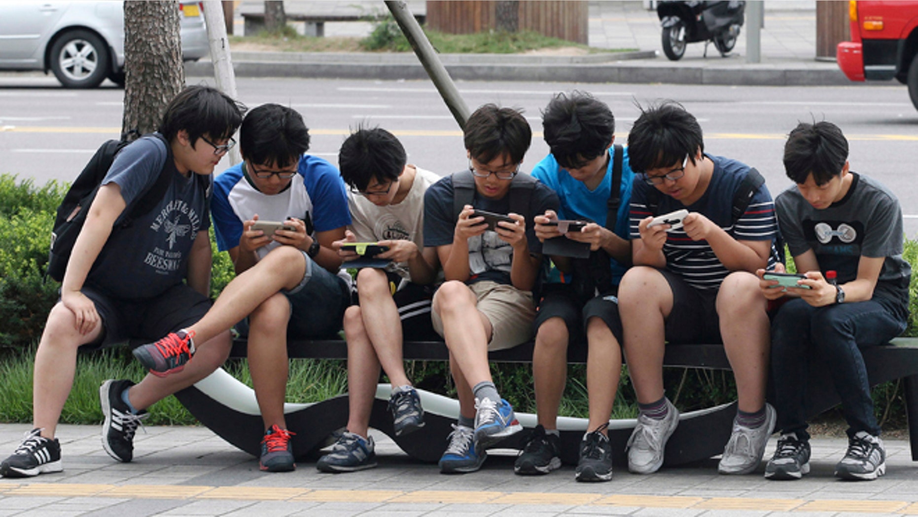 July 16, 2015: South Korean high school students play games on their smartphones on a bench on the sidewalk in Seoul, South Korea. The most widely used child surveillance app in South Korea is being quietly pulled from the market after security specialists raised serious concerns about the program's safety.