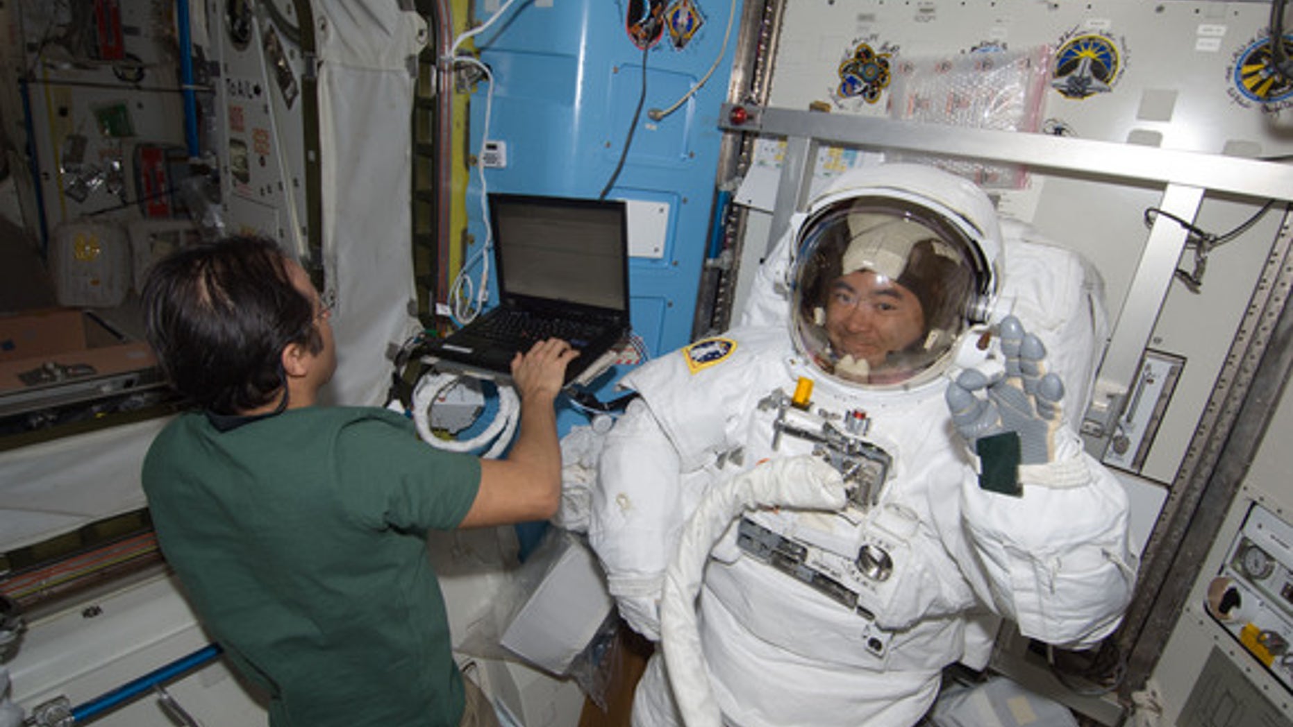 Japanese astronaut Akihiko Hoshide of JAXA waves while testing his spacesuit inside the International Space Station ahead of an Aug. 30, 2012 spacewalk with crewmate Sunita Williams of NASA. NASA astronaut Joe Acaba (left) assists.