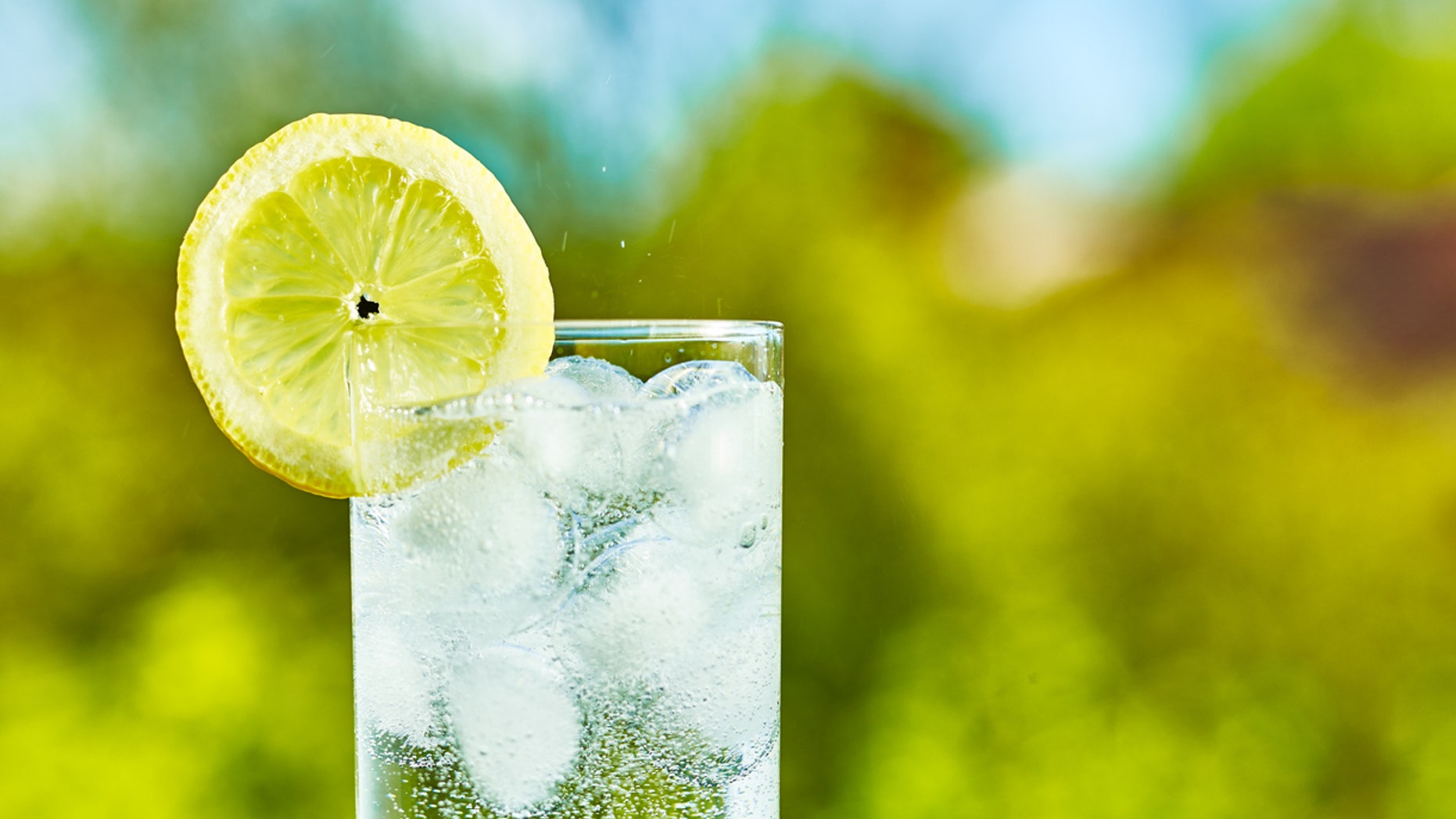 Sparkling water and lemon slice on glass with an ice, sunny day - narrow focus on middle of the glass