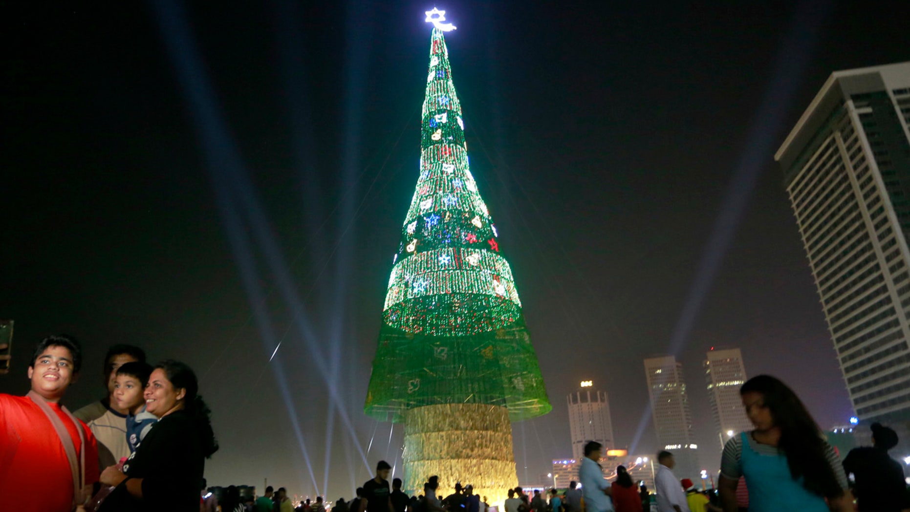 A Sri Lankan family takes photographs standing near an enormous artificial Christmas tree as others gather around it in Colombo, Sri Lanka, Saturday, Dec. 24, 2016.