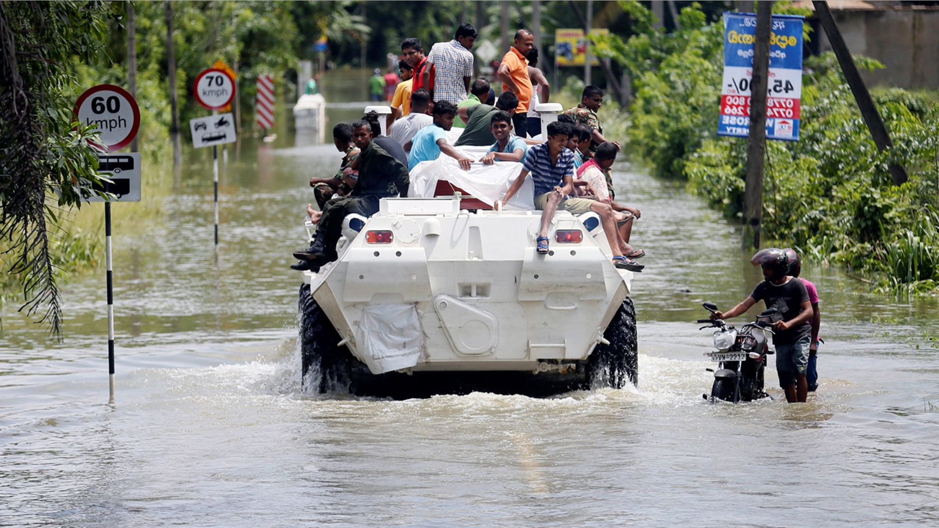 People are transported on top of an armoured personnel carrier on a flooded road as a man pushes his bike thorugh the water, in Bulathsinhala village, in Kalutara, Sri Lanka.