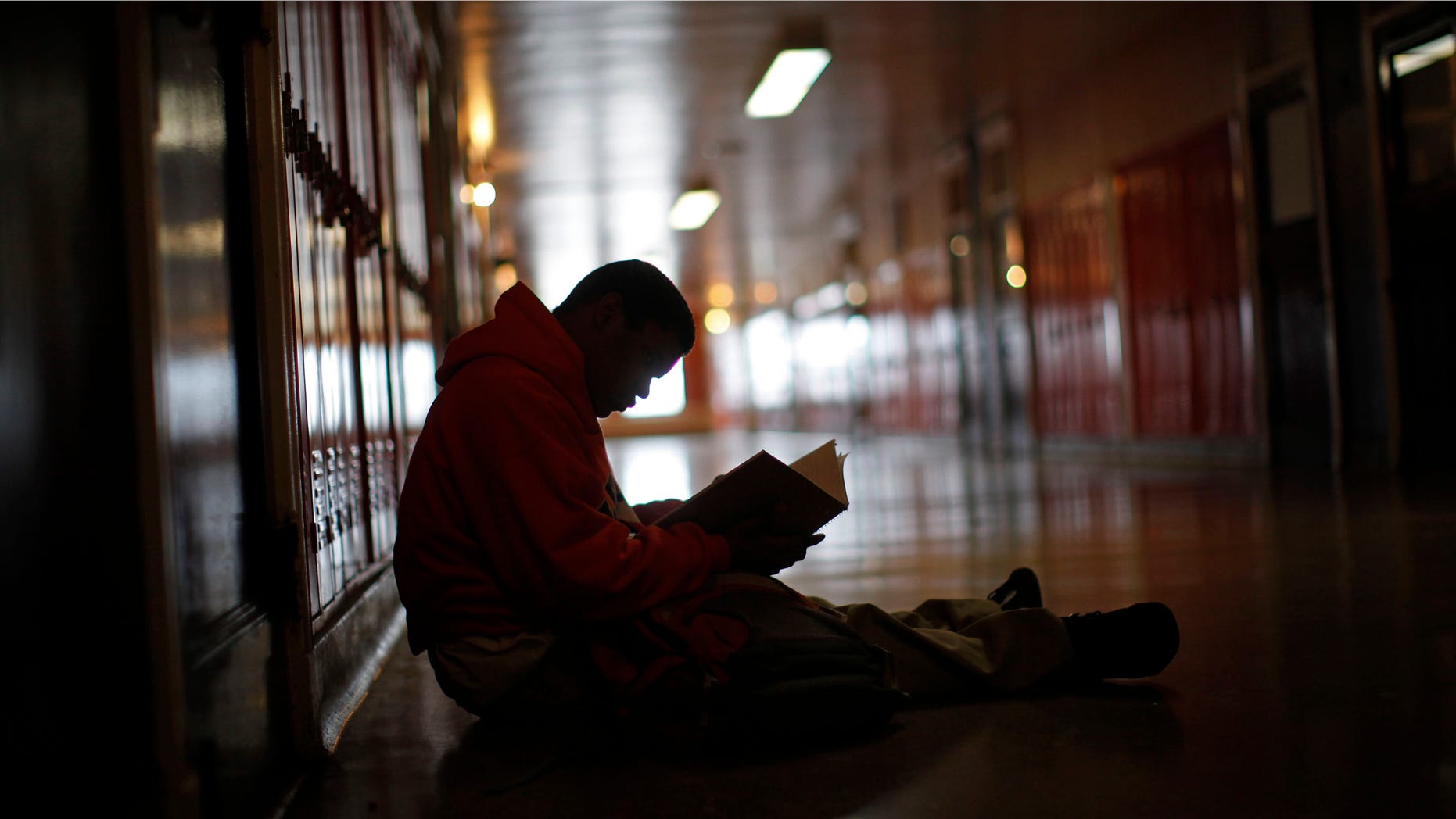 A student sits in the hallway as he looks through a text book.