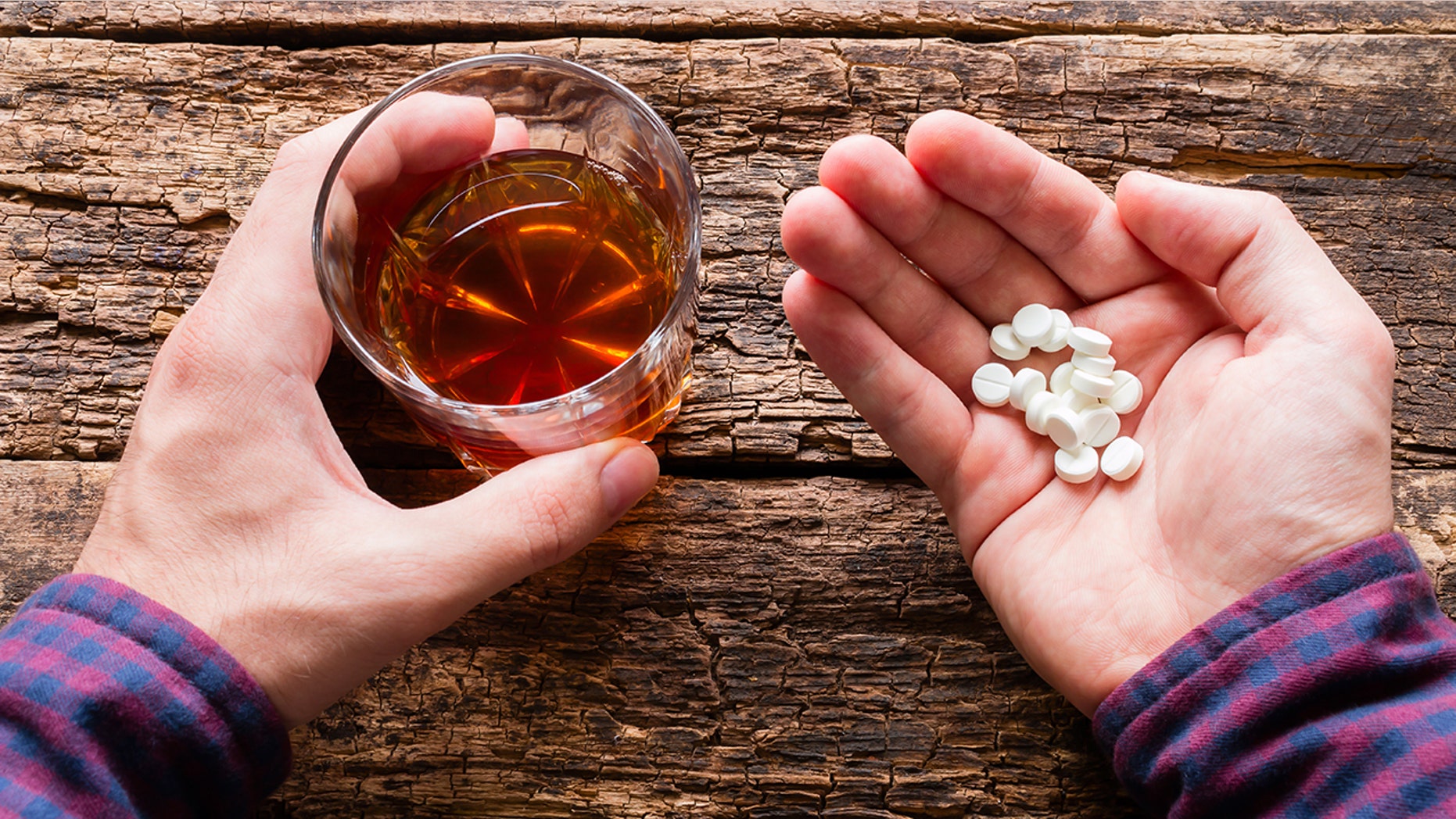 man holding a glass of alcohol and a handful of pills