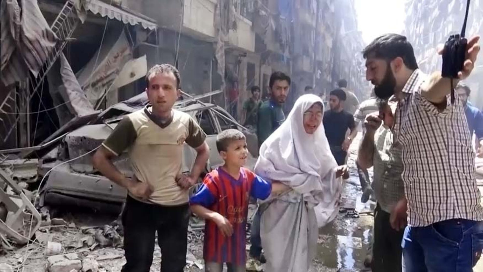In this image made from video and posted online from Validated UGC, a man leads a woman in tears and child out of the scene after airstrikes hit Aleppo, Syria, Thursday, April 28, 2016.