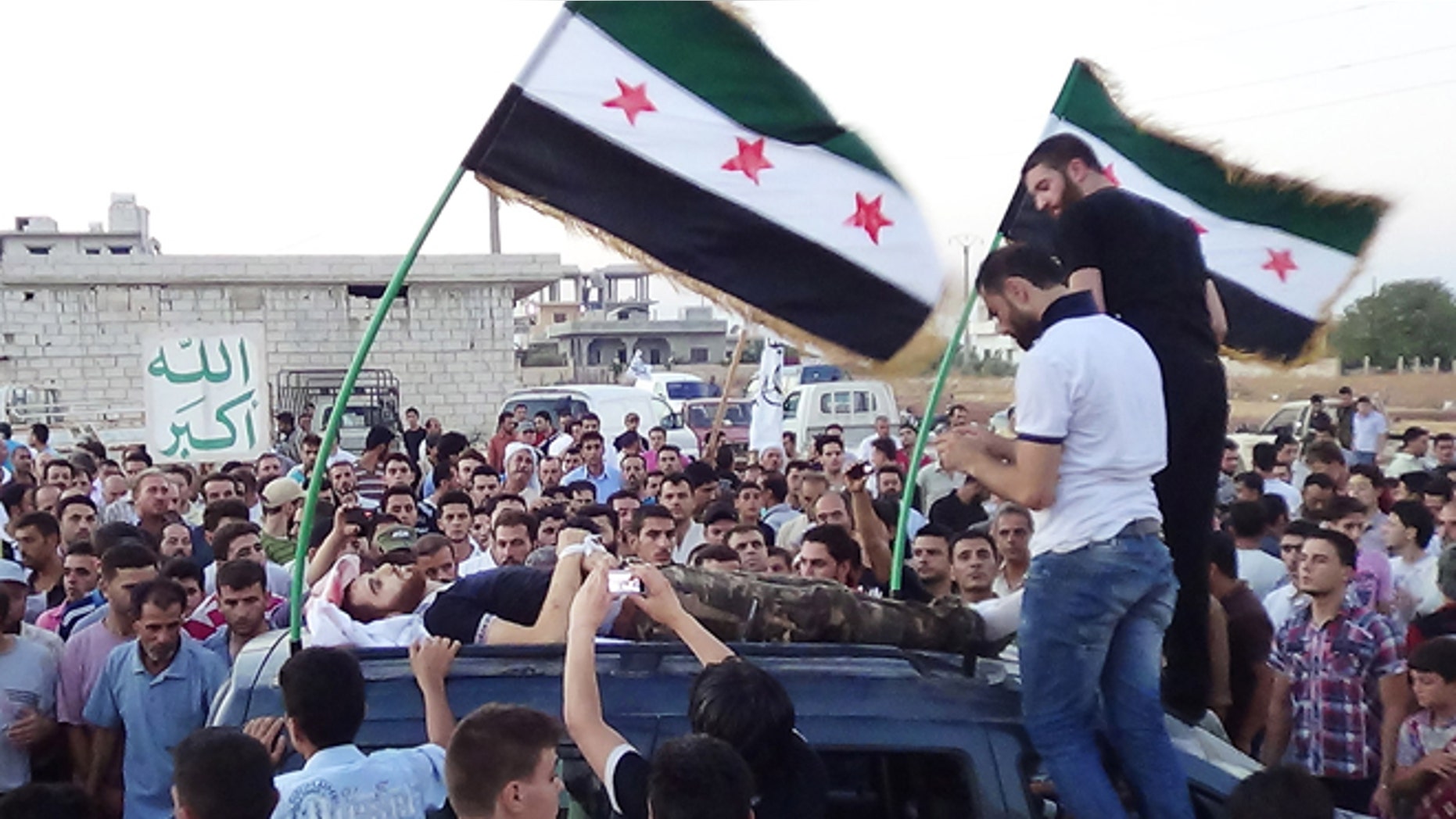 In this citizen journalism image provided by Shaam News Network SNN, taken on Tuesday, Aug. 7, 2012, Syrians attend the funeral procession of a man killed in Idlib province, Syria. Arabic, left, reads, "God is great."