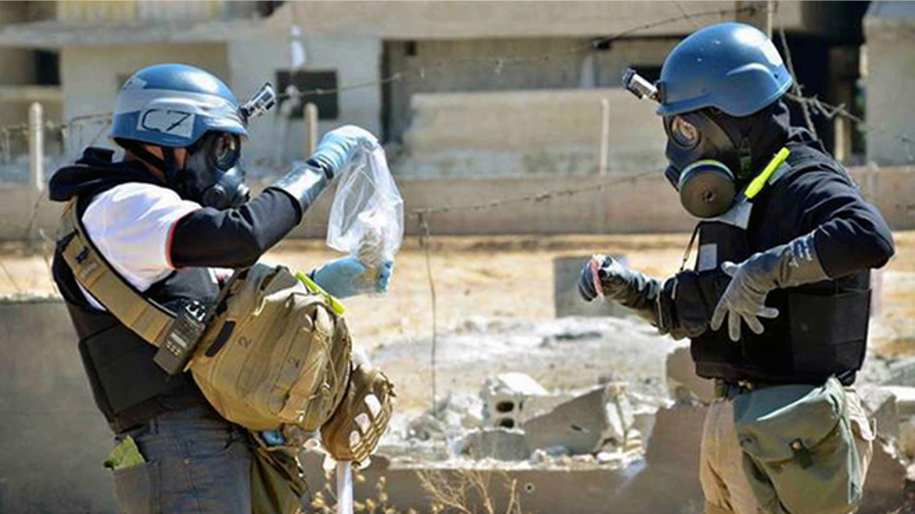 In this Aug. 28, 2013, file photo, a citizen journalism image provided by the United Media Office of Arbeen shows members of the United Nations investigation team take samples from sand near a part of a missile that is likely to be a chemical rocket, according to activists, in the Damascus countryside of Ain Terma, Syria.