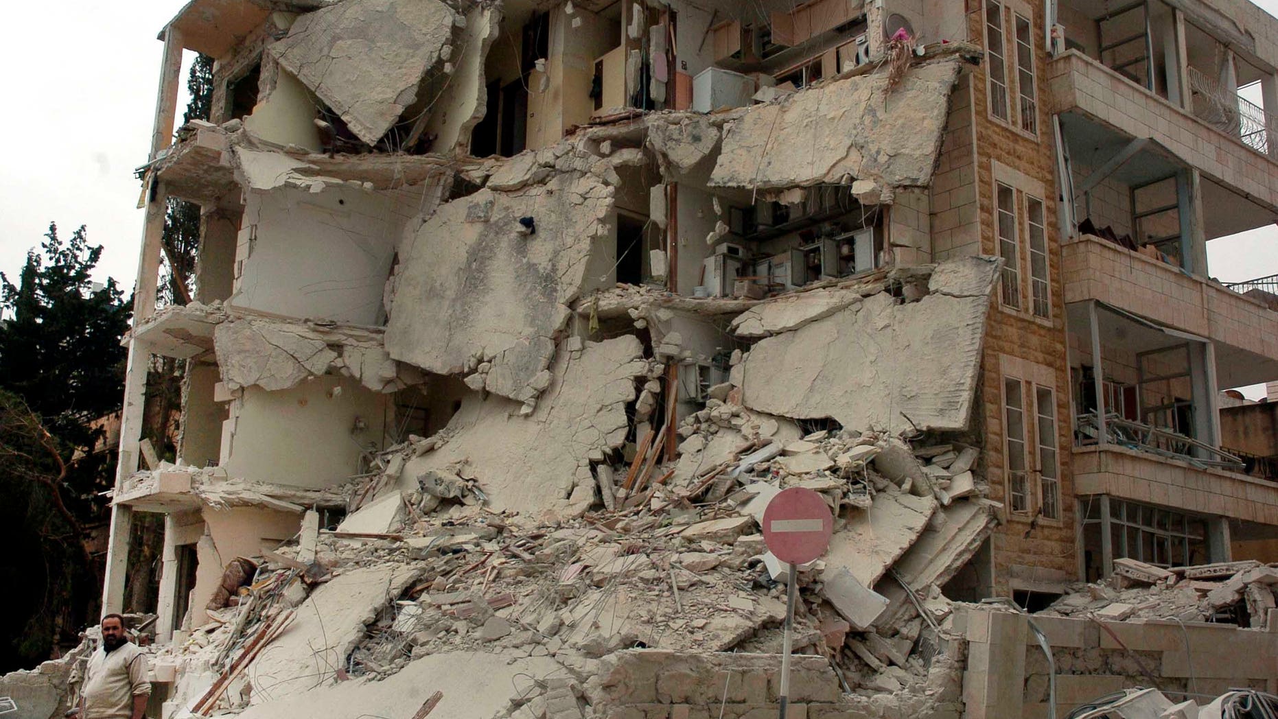 In this photo released by the Syrian official news agency SANA, a Syrian man, left, stands in front of a building that was damaged after two bombs exploded near a military compound, in the city of Idlib, northwestern Syria, Monday, April 30, 2012.
