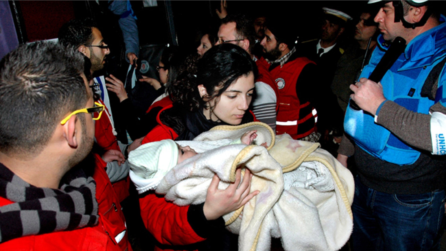 Feb. 10, 2014: In this photo released by the Syrian official news agency SANA, a Syrian Arab Red Crescent member in red uniform carries a baby on to a bus to evacuate the battleground city of Homs, Syria.