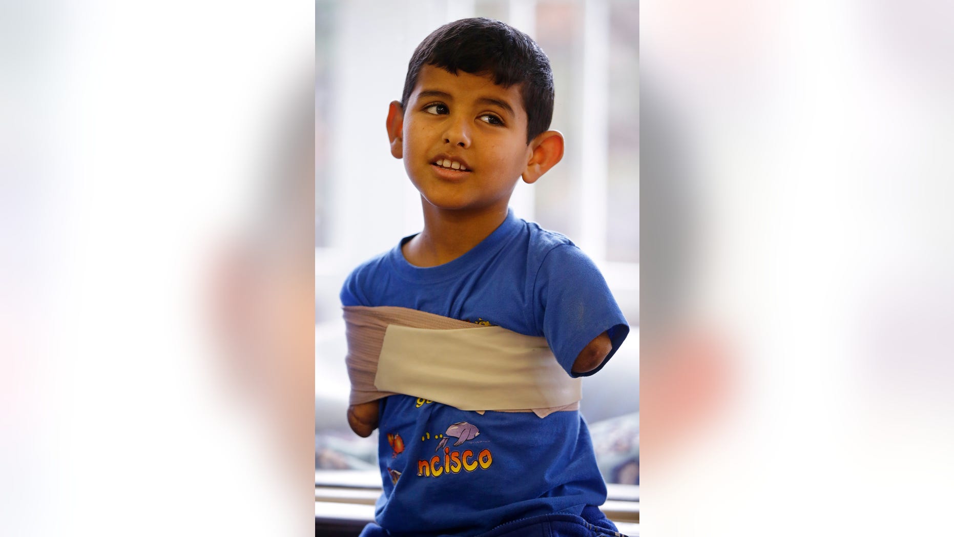 In this Friday, Dec. 18, 2015, photo Syrian refugee Ahmad Alkhalaf, 9, talks with his father and sponsors at a mosque in Sharon, Mass. Ahmad, who arrived in the Boston area this past summer for medical treatment, said he used to have restless nights when he would relive his mothers screams from the night a bomb killed three of his siblings and left him without arms. But those sounds, he said, have largely faded. (AP Photo/Stephan Savoia)