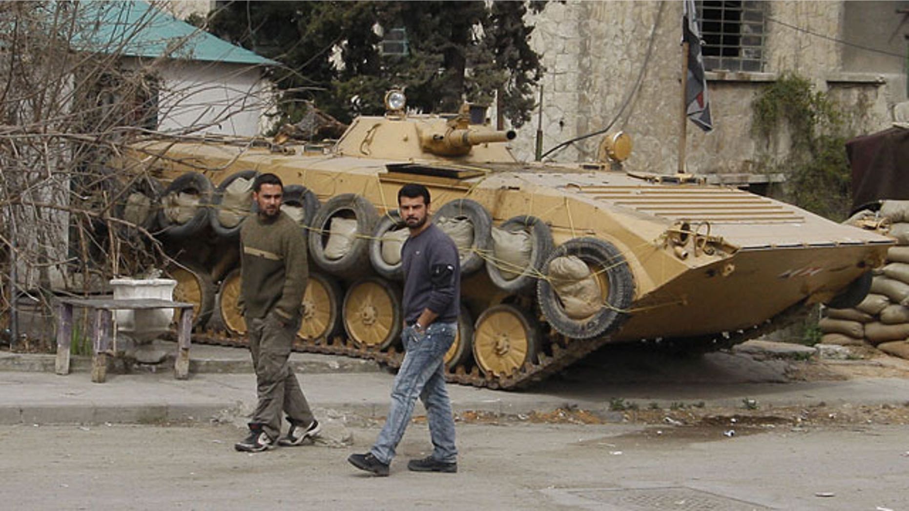 Feb. 15, 2012: In this photo taken on a government-organized tour for the media, Syrian citizens pass by a Syrian government army tank, in one of several suburbs of Damascus that saw heavy fighting between troops and defectors before Assad's forces retook the areas in late January, in Harasta suburb, Damascus, Syria.