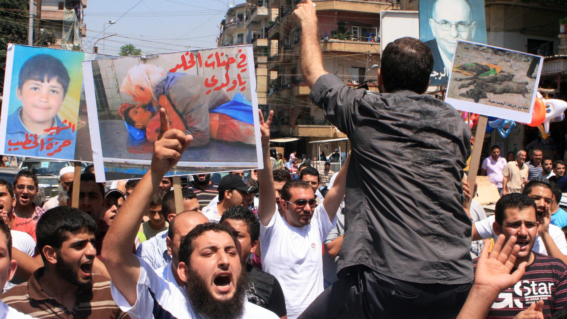 Lebanese protesters shout slogans as they carry banners in Arabic that read:" you are in heaven my son," center, "the martyr Hamza el-Khatib," left, and " Daraa mass graves," right, during a rally in solidarity with Syrian anti-government protesters in the northern city of Tripoli, Lebanon, Friday, July 15, 2011.