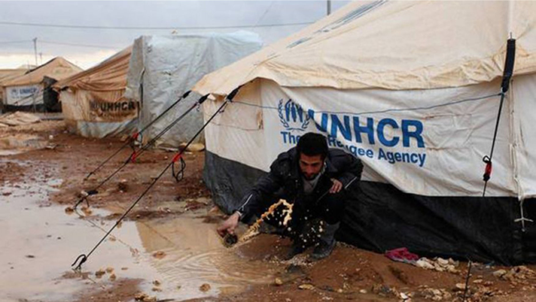 A Syrian refugee removes water and mud around his UN-supplied tent, at Zaatari Syrian refugee camp, near the Syrian border in Mafraq, Jordan.