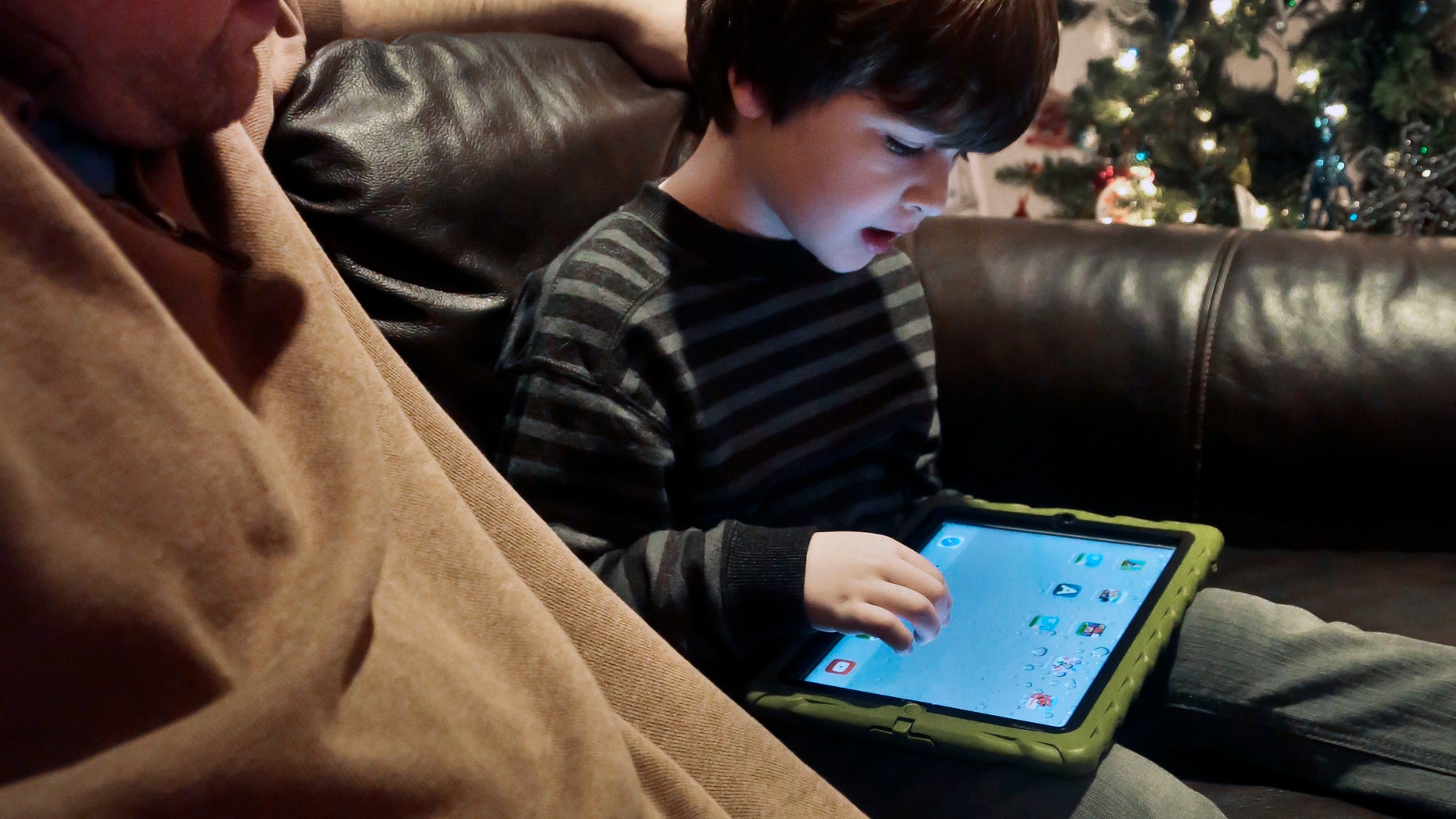 In this Dec. 3, 2013, photo, Adam Cohen watches as his son Marc, 5, uses a tablet at their home in New York. Tablets of all types are expected to rank among the top holiday gifts for children this year, but some experts and advocates question the educational or developmental benefits for youngsters. (AP Photo/Bebeto Matthews)
