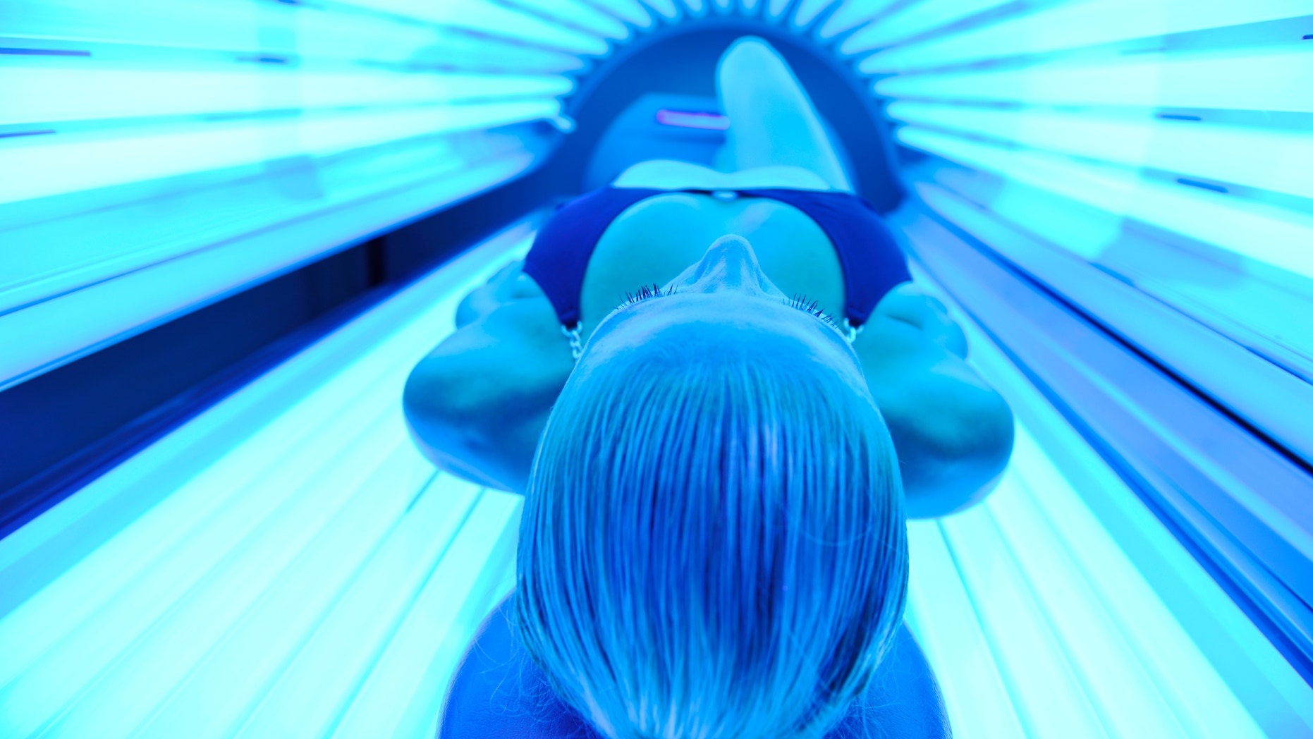 young woman at laying on solarium bed and get brown skin tone ready for summer