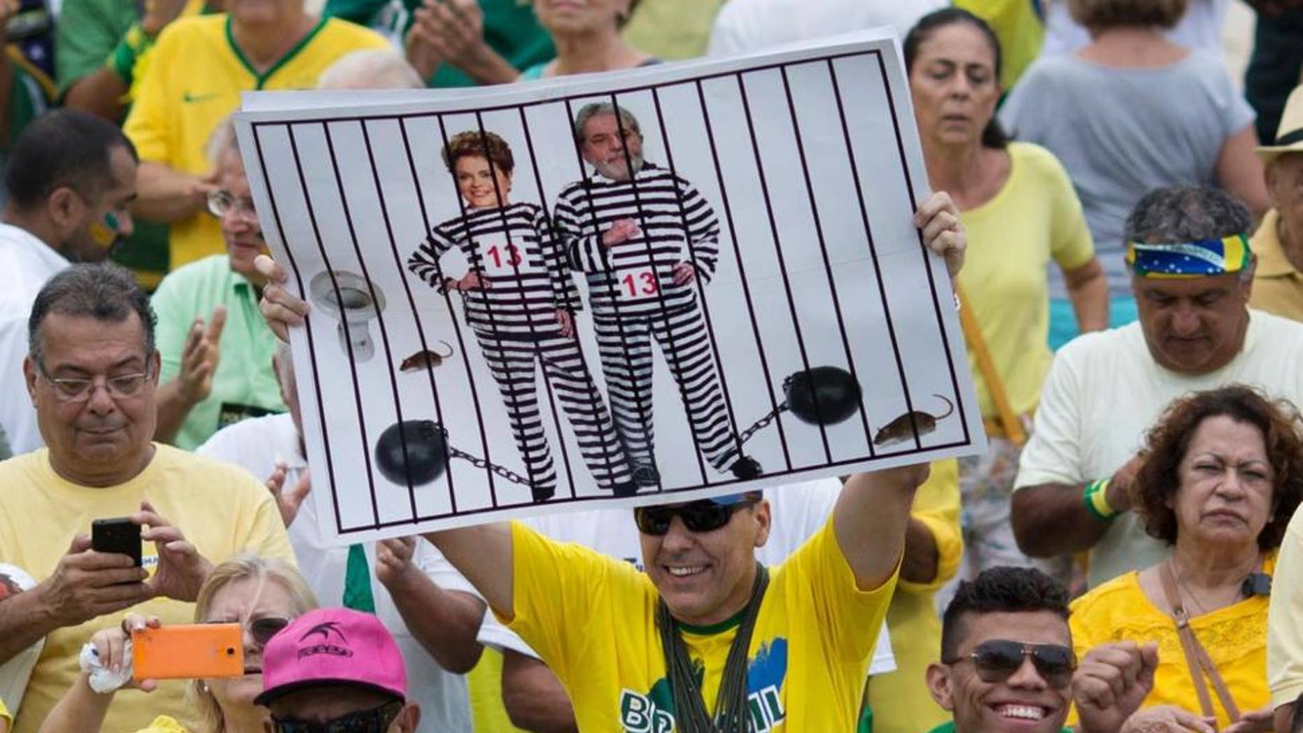 n this March 13, 2016 file photo, a demonstrator holds a poster with the photo of Brazilian president Dilma Rousseff and former President Luiz Inacio Lula da Silva in prison stripes during a protest on Copacabana beach in Rio de Janeiro, Brazil.