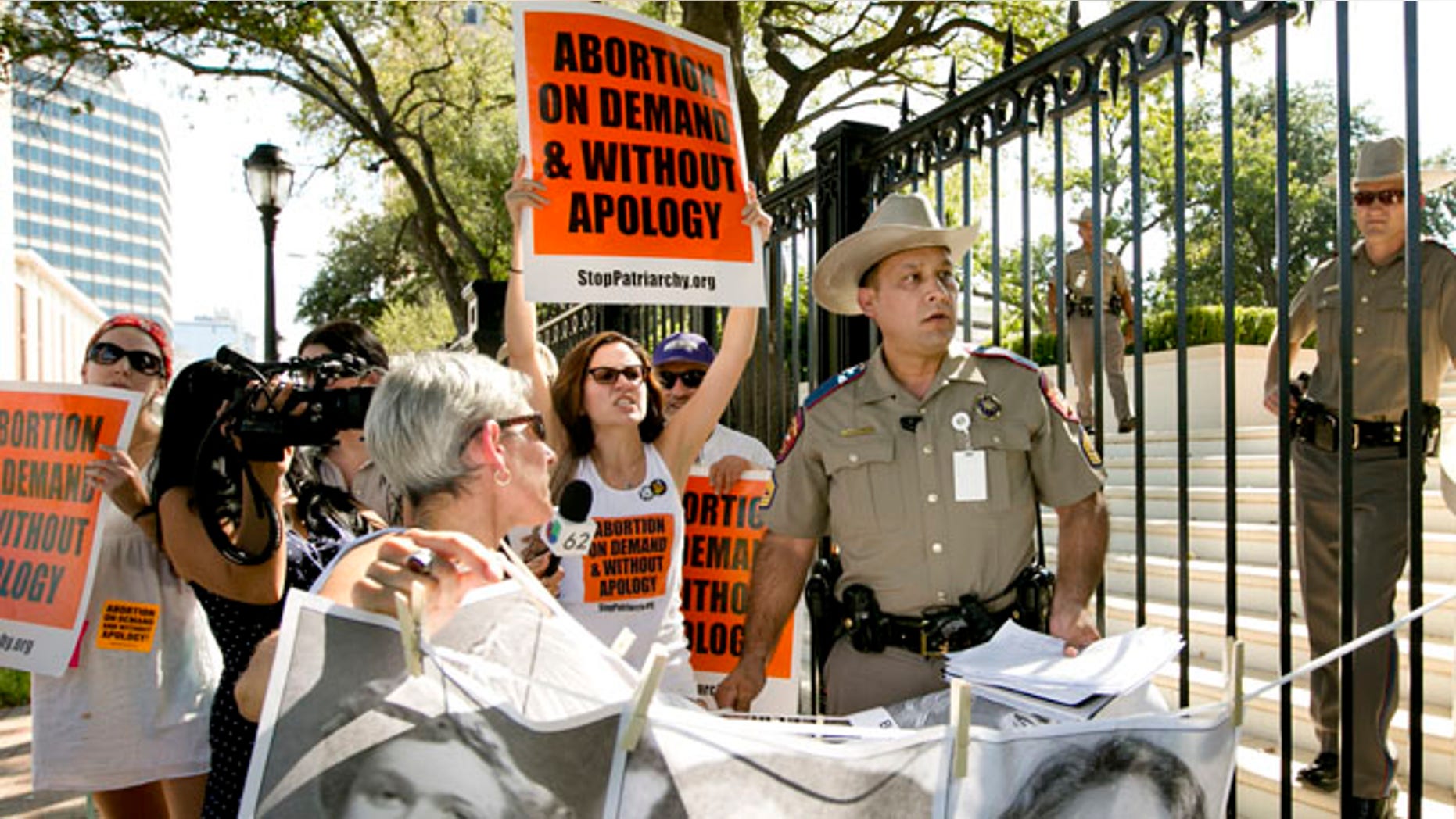 Aug 25, 2014: Pro-abortion rights activists chant slogans while a Texas Department of Public Safety trooper removes their signs from the gate of the Governor's Mansion in Austin, Texas.