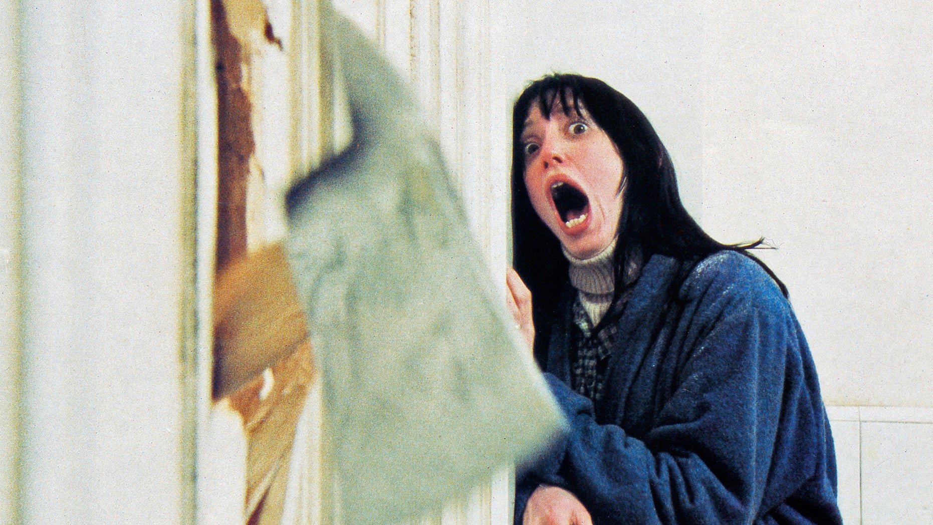 actress Shelley Duvall, recoils in shock as her husband chops through the bathroom door with a fire axe in a scene from 'The Shining', directed by Stanley Kubrick