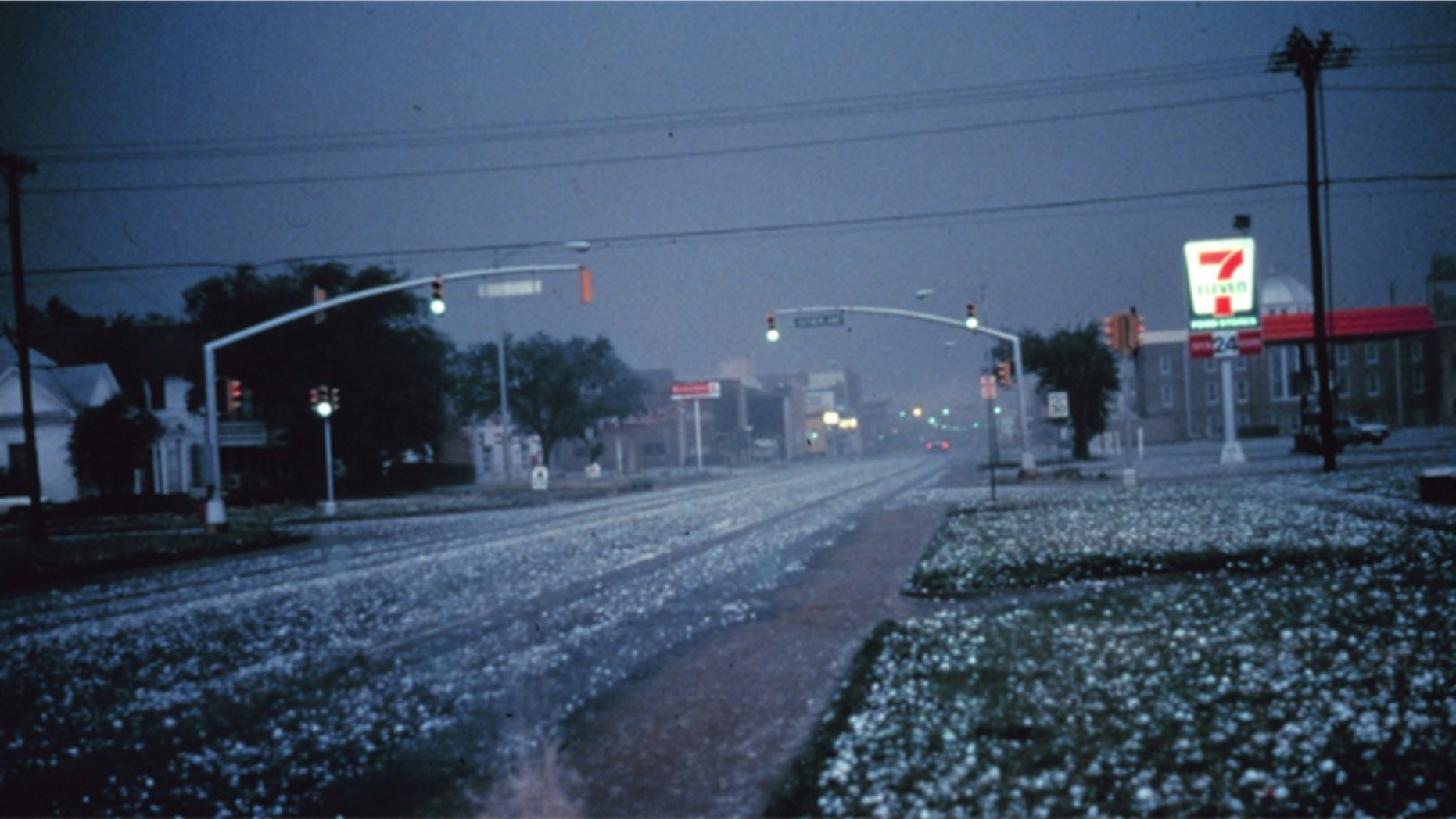 Large hail collects on streets and grass during severe thunderstorm. Larger stones appear to be nearly 2 to 3 inches in diameter.