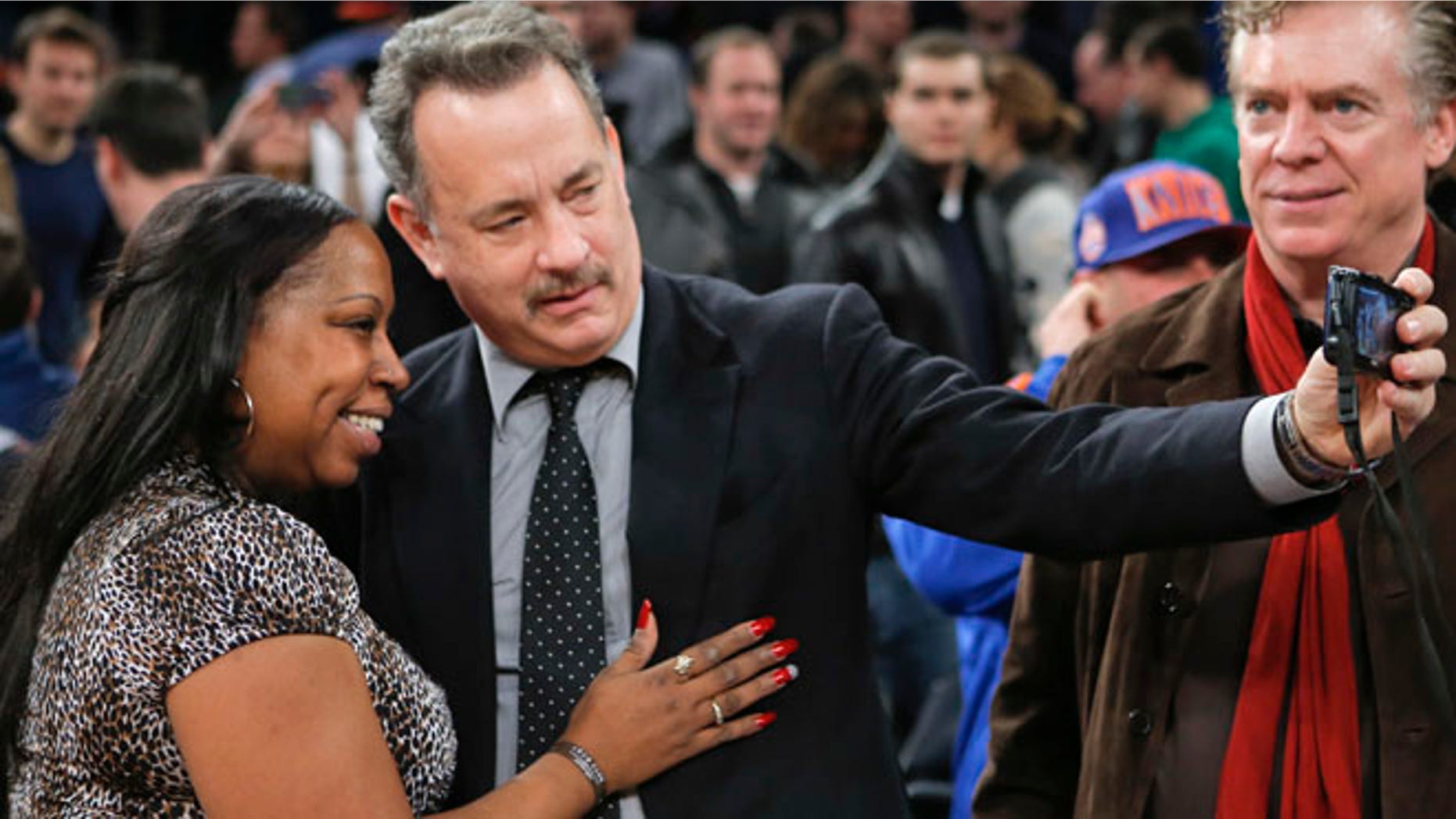 Actor Tom Hanks (C) tries to take a picture with a fan after the New York Knicks played the Los Angeles Clippers in their NBA basketball game at Madison Square Garden in New York, February 10, 2013. Actor Christopher McDonald (R) watches. REUTERS/Ray Stubblebine (UNITED STATES - Tags: SPORT BASKETBALL) - RTR3DLLE