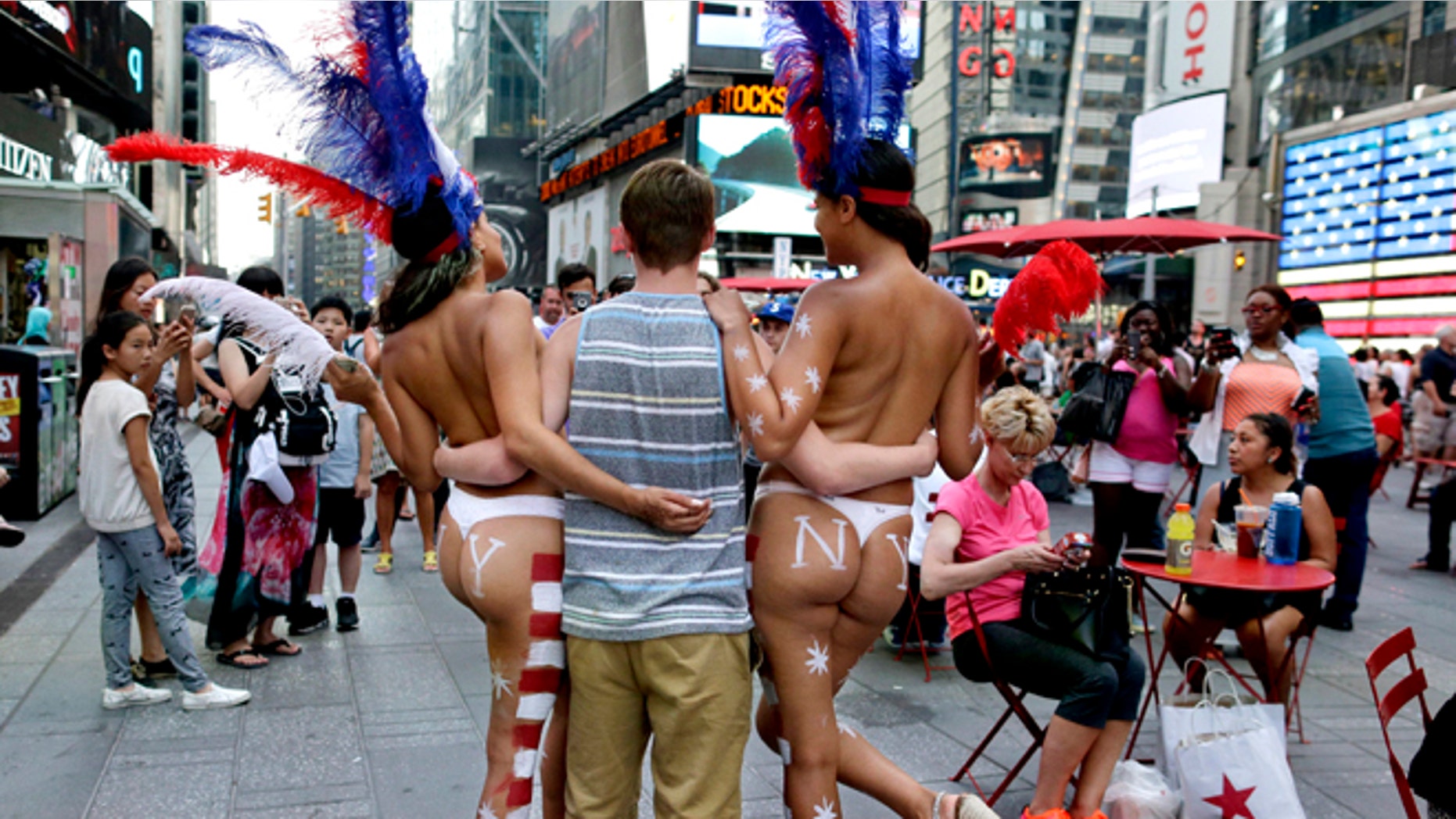 July 28, 2015: a tourist poses for a photo with two women clad in thongs and body paint in Times Square, in New York. (AP)
