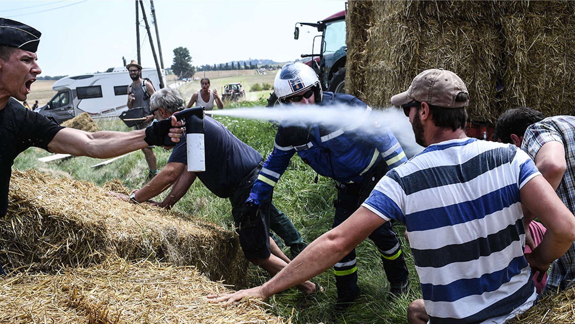 A gendarme, left, sprays tear gas at protesters as other gendarmes remove haystacks from the route of the Tour de France.