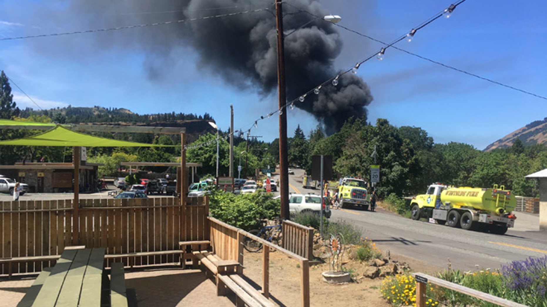 In this photo provided by Silas Bleakley, a train towing cars full of oil sends up a plume of smoke after derailing Friday, June 3, 2016, near Mosier, Ore. The accident happened just after noon about 70 miles east of Portland. It involved eight cars filled with oil, and one was burning. Highway 84 was closed for a 23-mile stretch between The Dalles and Mosier and the radius for evacuations was a half-mile. (Silas Bleakley via AP)
