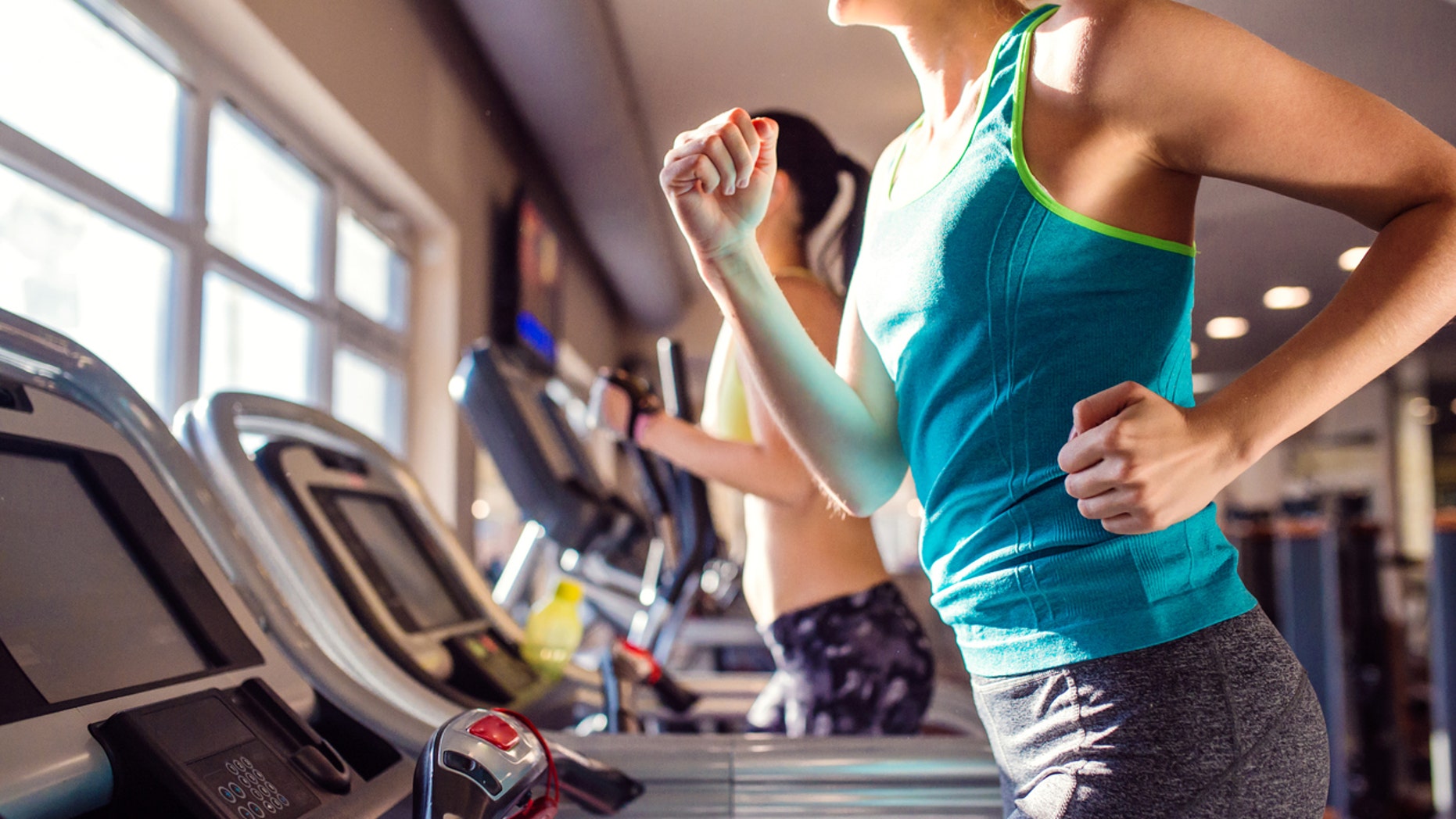 Two attractive fit women running in sports clothes on treadmills in modern gym