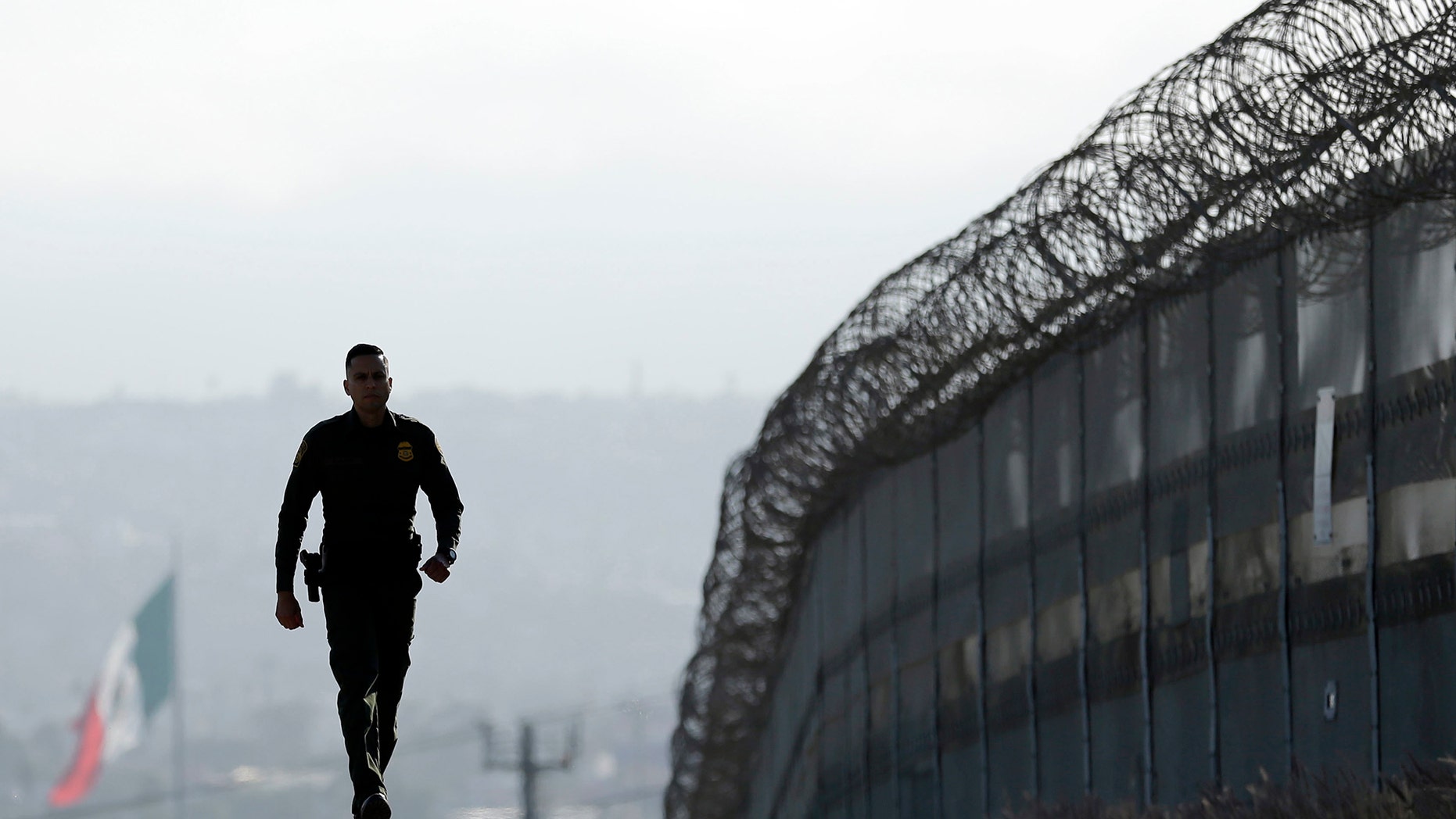 Border Patrol agent Eduardo Olmos walks near the secondary fence separating Tijuana, Mexico.
