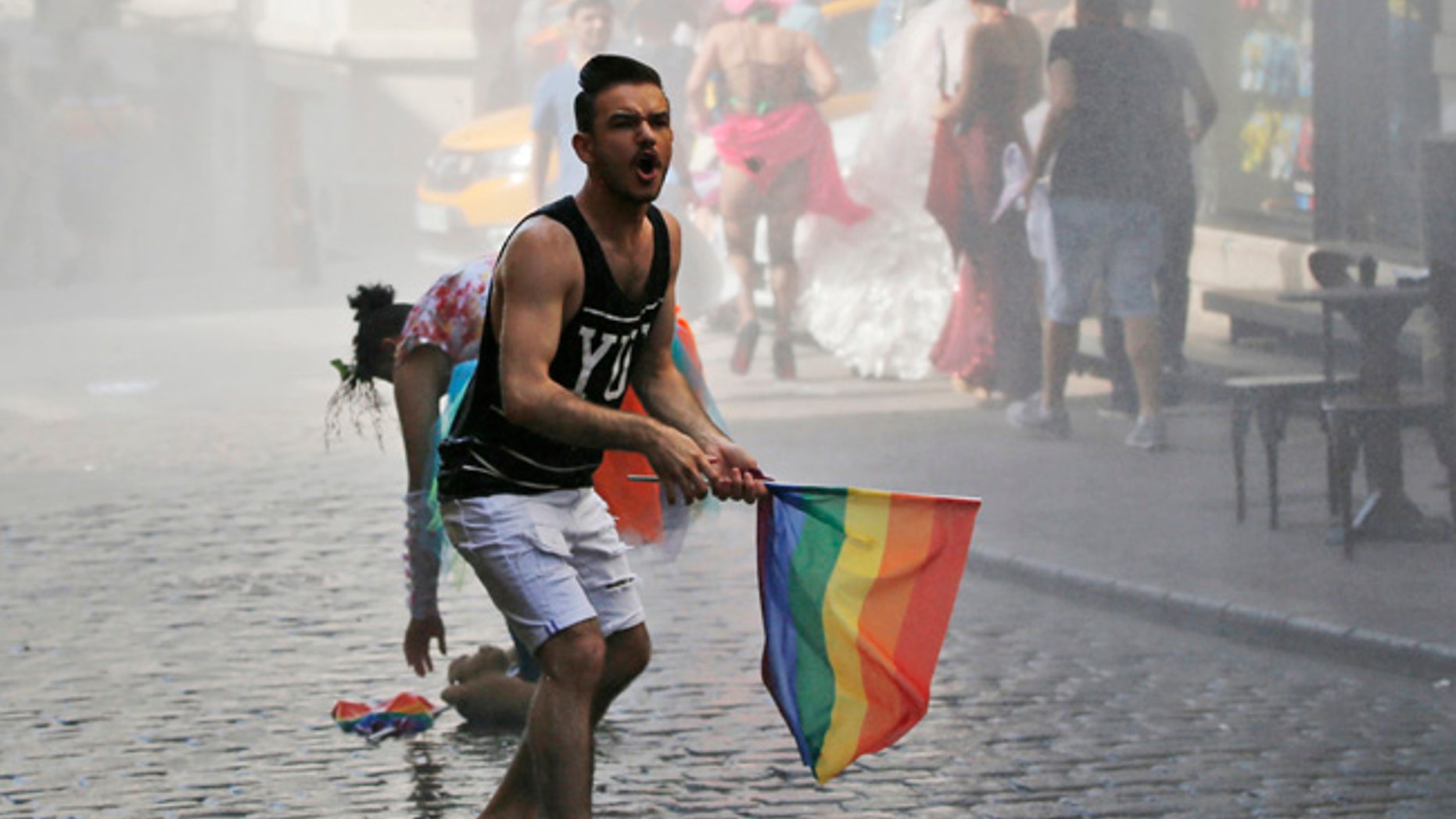 FILE - In this Sunday, June 28, 2015 file photo, a participant of the Pride Week march in Istanbul, reacts as others flee after Turkish police use a water canon to disperse them. For several years, Pride Week in Istanbul attracted tens of thousands of participants, making it one of largest gatherings celebrating gay, lesbian and transgender rights and diversity in the Muslim world. That changed suddenly in 2015, when authorities, citing security concerns, banned gay and trans-gender pride events chasing away shocked participants trying to converge on central Taksim Square with tear gas and water cannons. (AP Photo/Emrah Gurel, File)