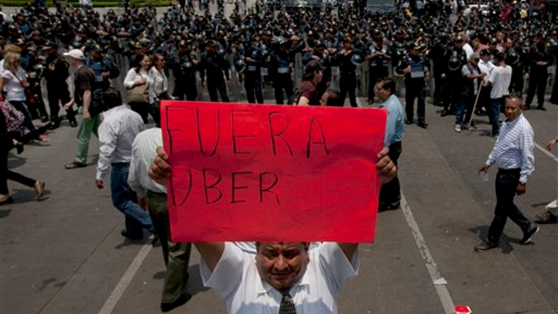 A man holds a sign the reads in Spanish "Uber Out" in front of a phalanx of riot police as thousands of taxi drivers blocked the main streets in Mexico City, Monday, May 25, 2015. The Mexican taxi drivers' union called for a protest against unlicensed and UBER taxis working in Mexico City. (AP Photo/Marco Ugarte)