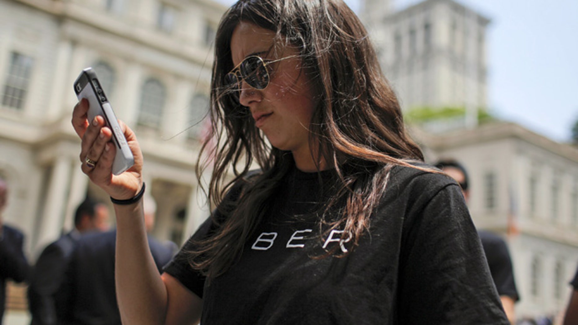 FILE: A woman wearing a Uber T-shirt checks her phone while Uber riders and driver-partners take part in a rally on the steps of New York City Hall.