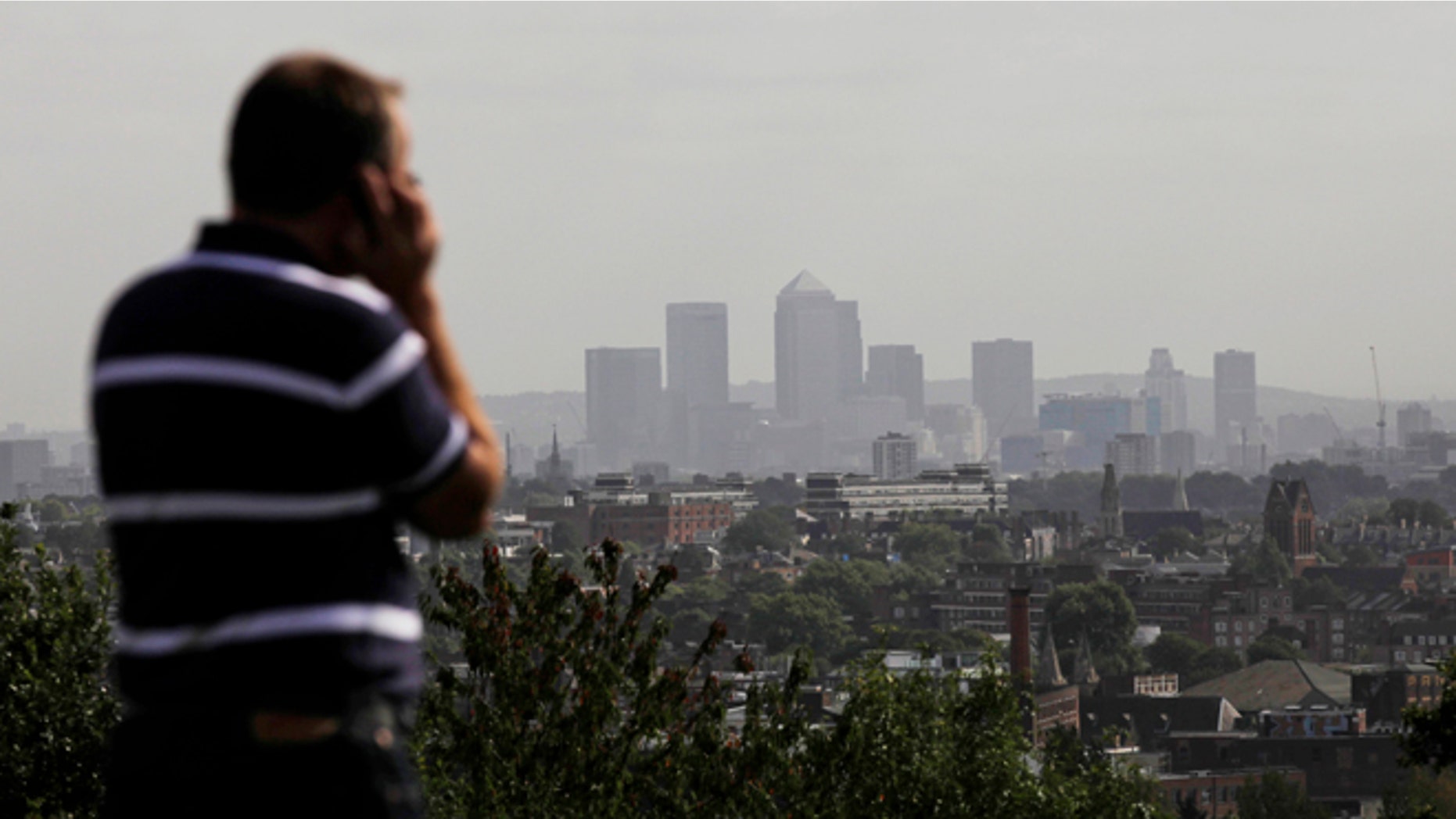 FILE In this Friday, Sept. 23, 2011 file photo a man talks on a mobile phone as the hi-rise buildings of the banks based in the Canary Wharf business district are seen in the distance from Parliament Hill on Hampstead Heath in London.