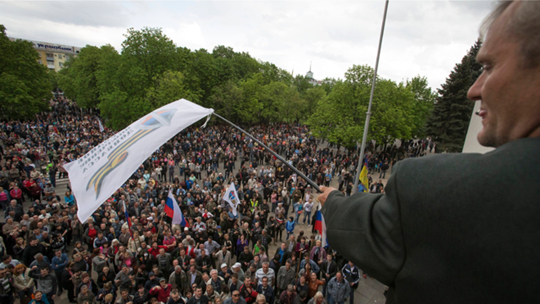 April 29, 2014: A Pro-Russian activist waves a Donbas Republic flag over a crowd celebrating the capture of an administration building in the center of Luhansk, Ukraine, one of the largest cities in Ukraine's troubled east, as demonstrators demand greater autonomy for Ukraine's regions.