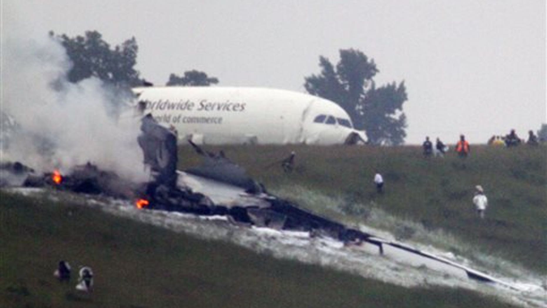 Debris burns as a UPS cargo plane lies on a hill at Birmingham-Shuttlesworth International Airport after crashing on approach, Wednesday, Aug. 14, 2013, in Birmingham, Ala. Toni Herrera-Bast, a spokeswoman for Birmingham's airport authority, says there are no homes in the immediate area of the crash. (AP Photo/Hal Yeager)