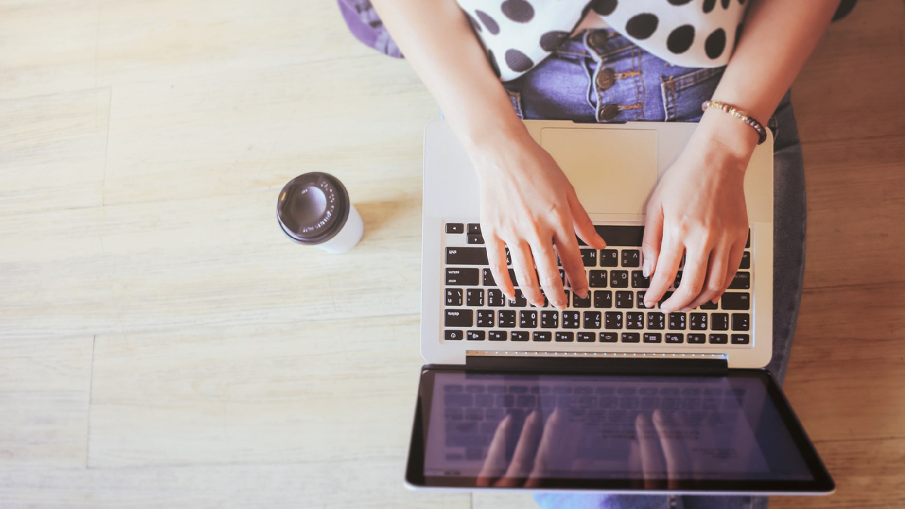 Top view of laptop in girl's hands sitting on wooden floor with coffee