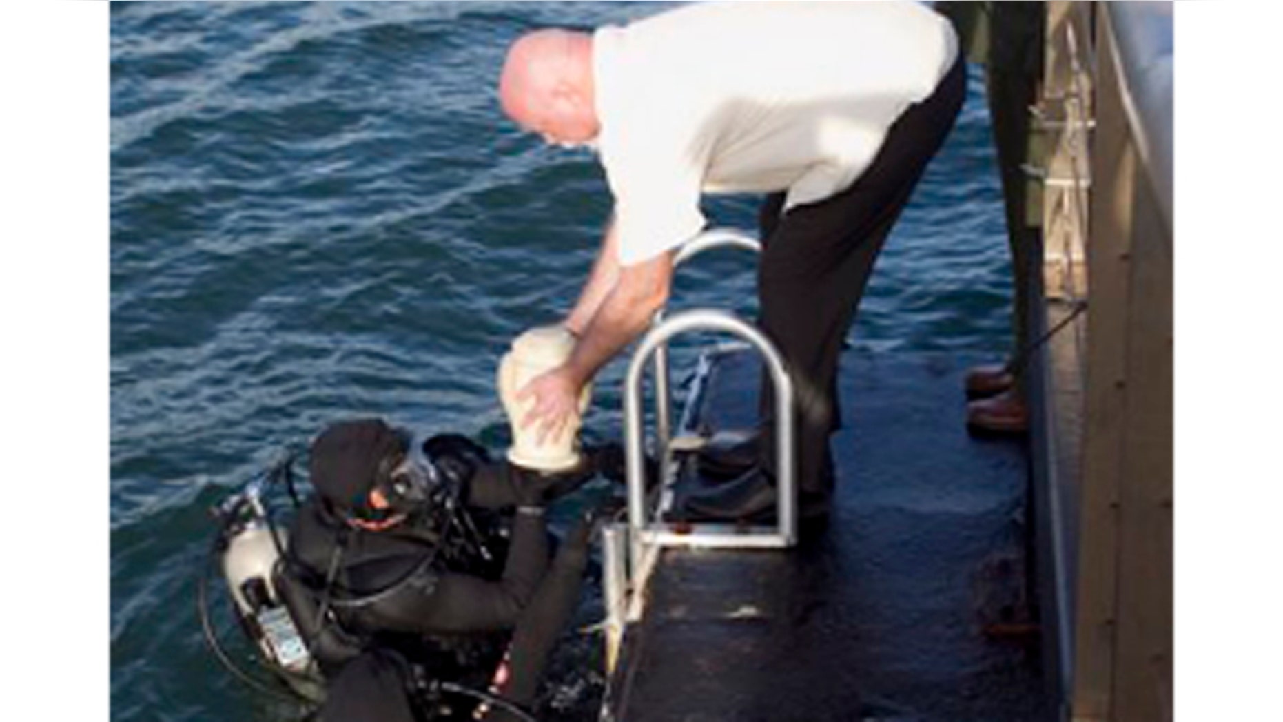 Dec. 23, 2011: As National Parks Historian Daniel Martinez salutes, Jerry Cabiness, center, hands the remains of his father to divers to be interred inside the USS Arizona in Honolulu.