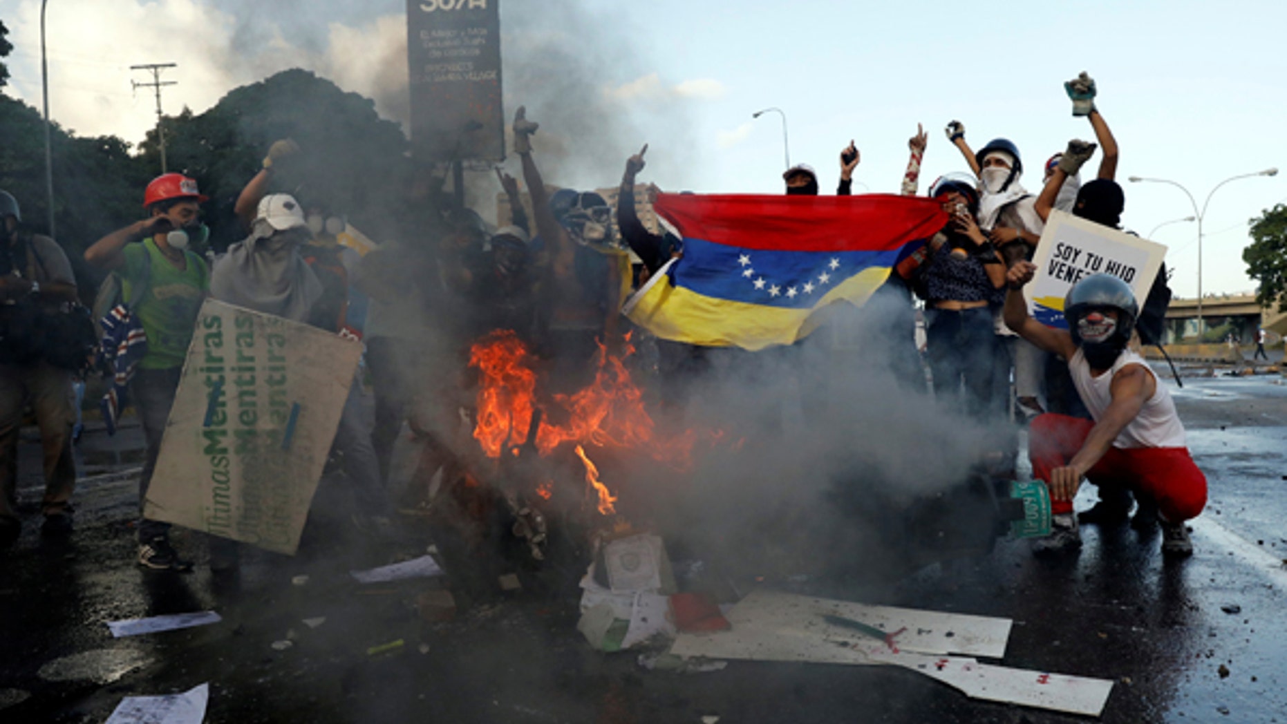 Opposition supporters hold a Venezuelan national flag in front of a burning riot security force motorcycle during clashes at a rally against Venezuelan President Nicolas Maduro's government in Caracas, Venezuela June 22, 2017. REUTERS/Carlos Garcia Rawlins - RTS189Z3