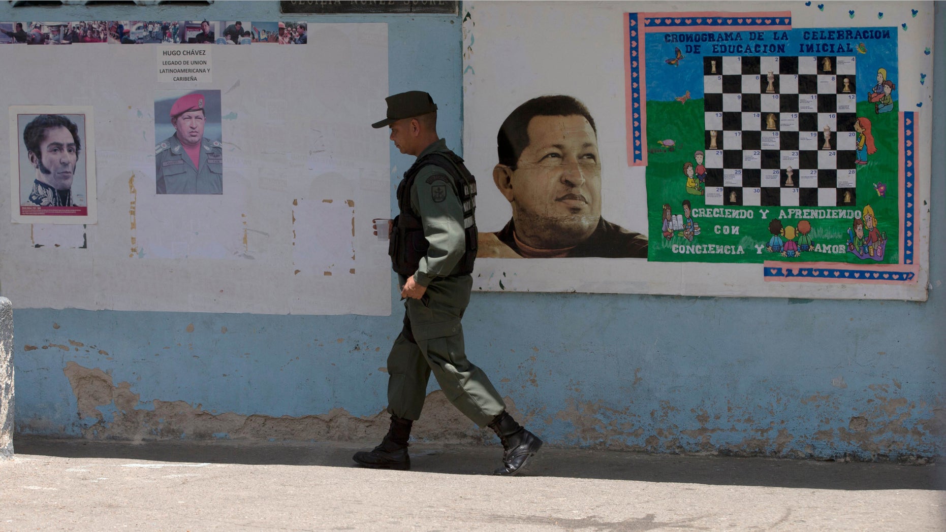 A Bolivarian National Guards officer walks near images of the late Venezuelan President Hugo Chavez and Independence hero Simon Bolivar, left, at a poll station in Caracas, Venezuela, Sunday, May 17, 2015. Venezuelans are voting to select the opposition leaders who will run against the ruling socialist partyâs candidates in upcoming legislative elections thought to be government criticsâ first chance at an electoral victory in years. (AP Photo/Fernando Llano)
