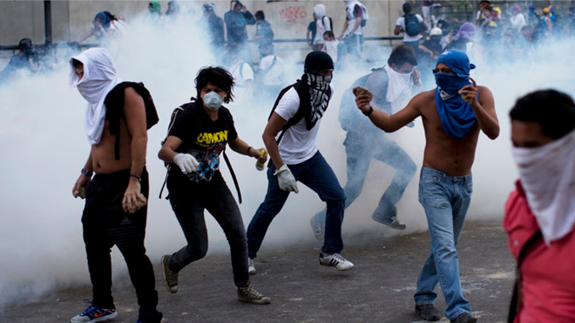 Feb. 22, 2014: A group of masked men run for cover after riot police launched tear gas in Caracas, Venezuela.