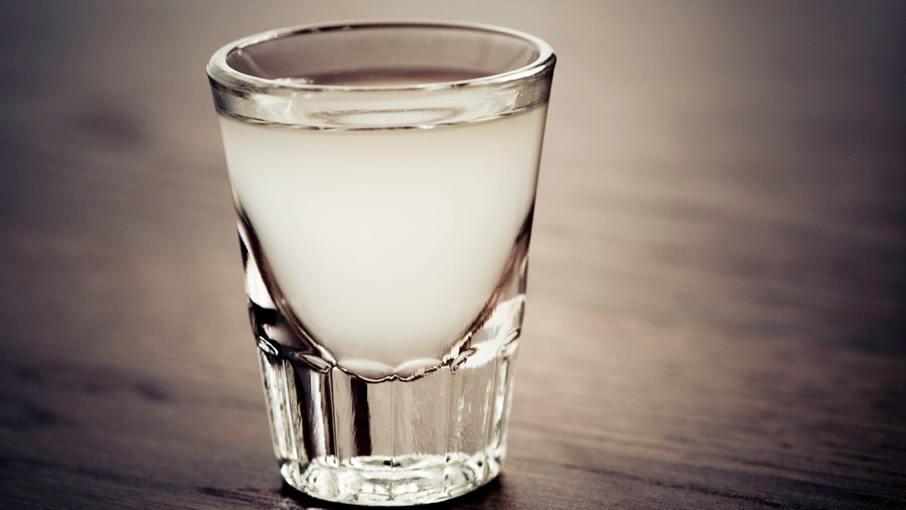 "Shot glass full of a light colored alcoholic drink. The drink could be a lemon drop or lemon juice with vodka, gin, rum, or tequila."