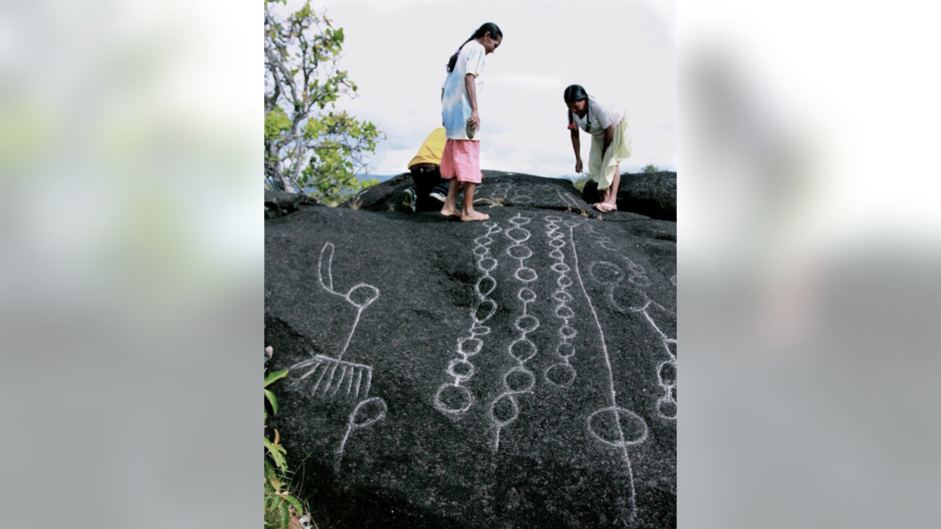 Two Wapishana women maintain traditional rock carvings at a spiritual site.