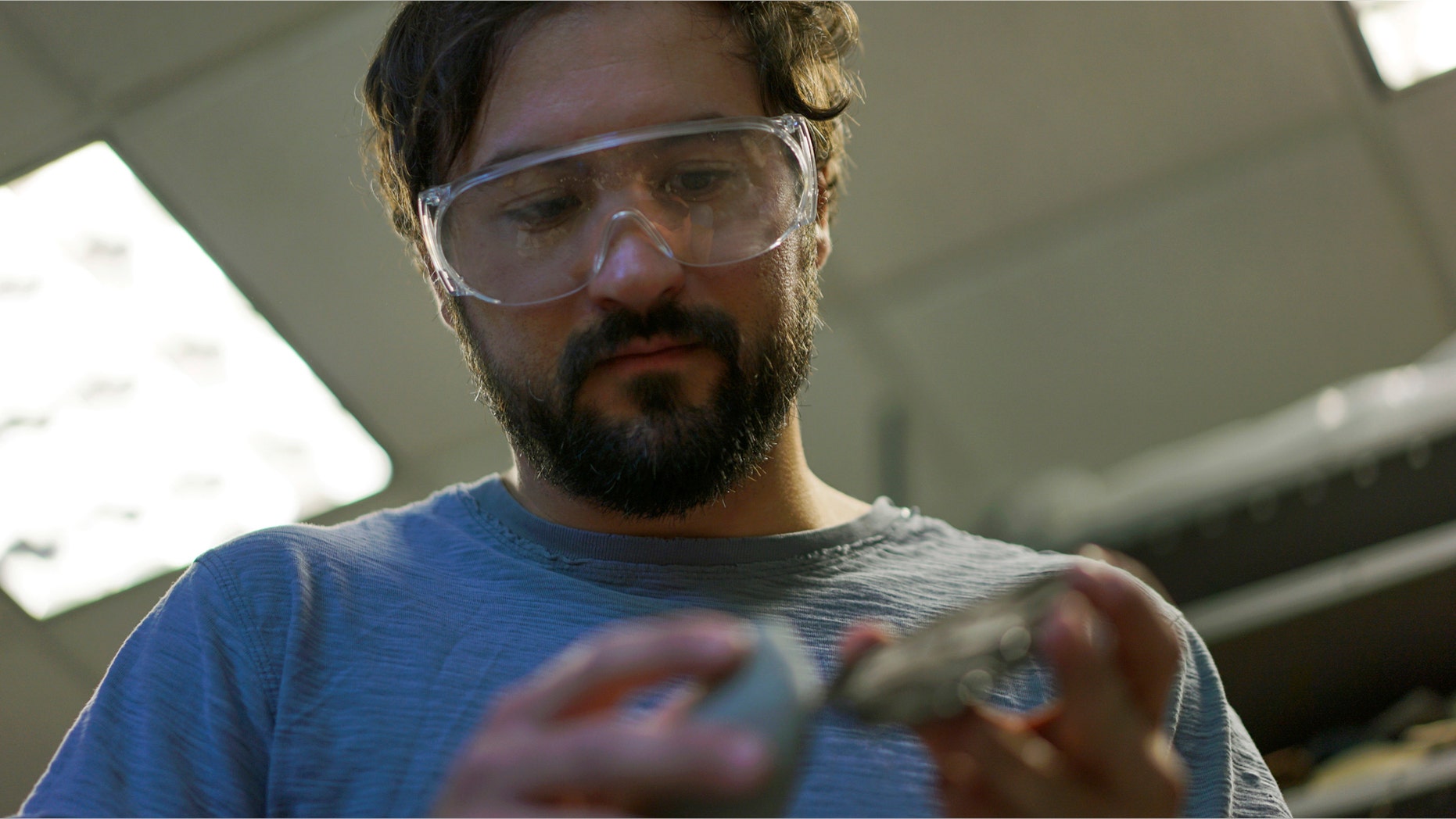 In this June 1, 2017, photo, Metin Eren, an archaeologist at Kent State University, looks at a newly chipped flake of obsidian in Kent, Ohio. Eren runs a newly-opened laboratory which makes replicas of ancient arrows, knives, and pottery to be shot, crushed, and smashed. It's allowing researchers to learn about engineering techniques of the first native Americans without destroying priceless genuine relics in the process. (AP Photo/Dake Kang)