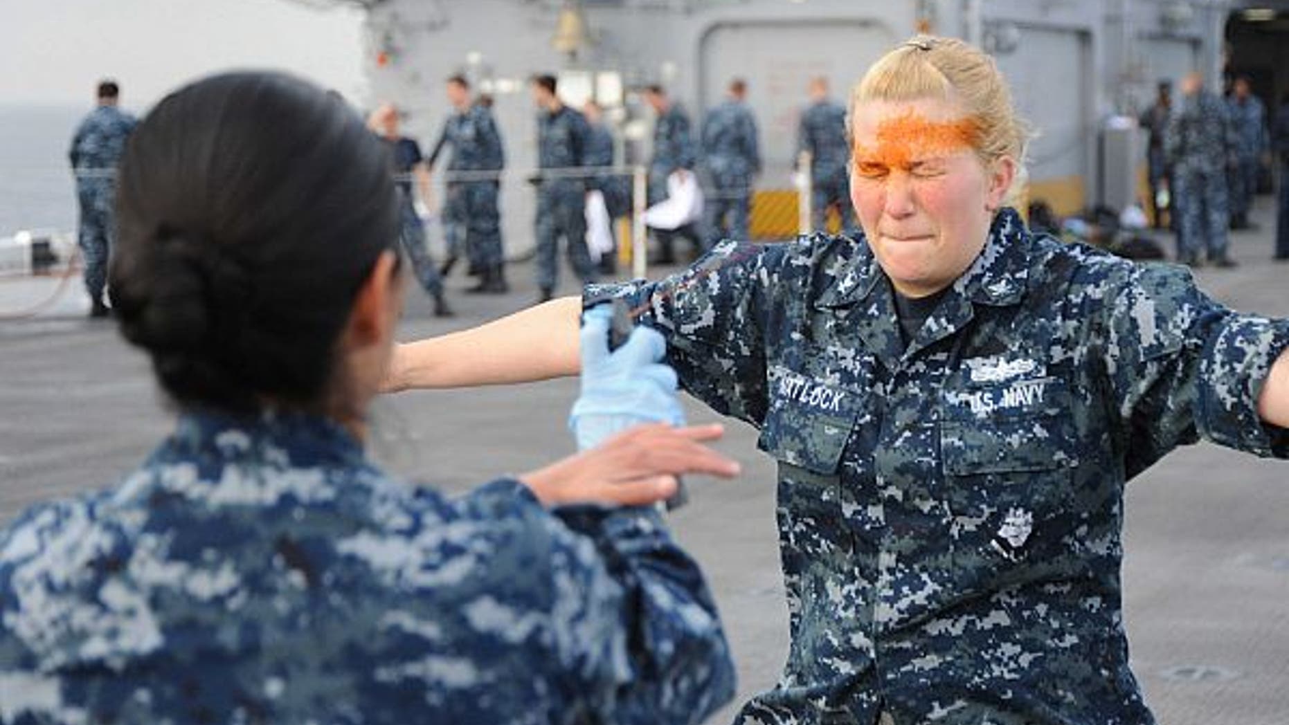 Master-at-Arms 1st Class Cathy Garcia sprays pepper spray into the eyes of Electronics Technician 3rd Marie Matlock.