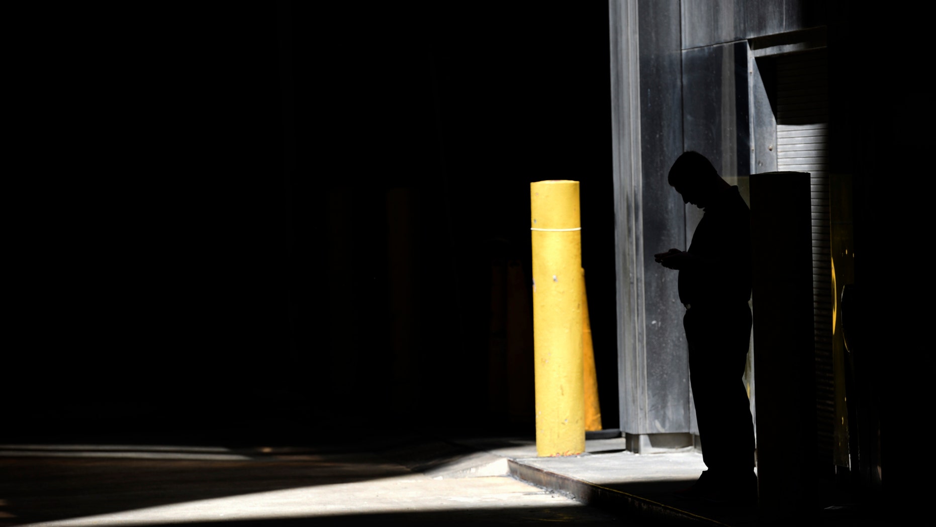 FILE- In this June 6, 2017, file photo, a man checks his phone in an alley in downtown Chicago. A security researcher says a website flaw at a U.S. company could have allowed anyone to pinpoint the location of nearly any cellphone in the United States. The lapse at LocationSmart, a company that gathers real-time data on cellular wireless devices, is the latest to highlight how little protection consumers have from trafficking in data about their location. (AP Photo/G-Jun Yam, File)
