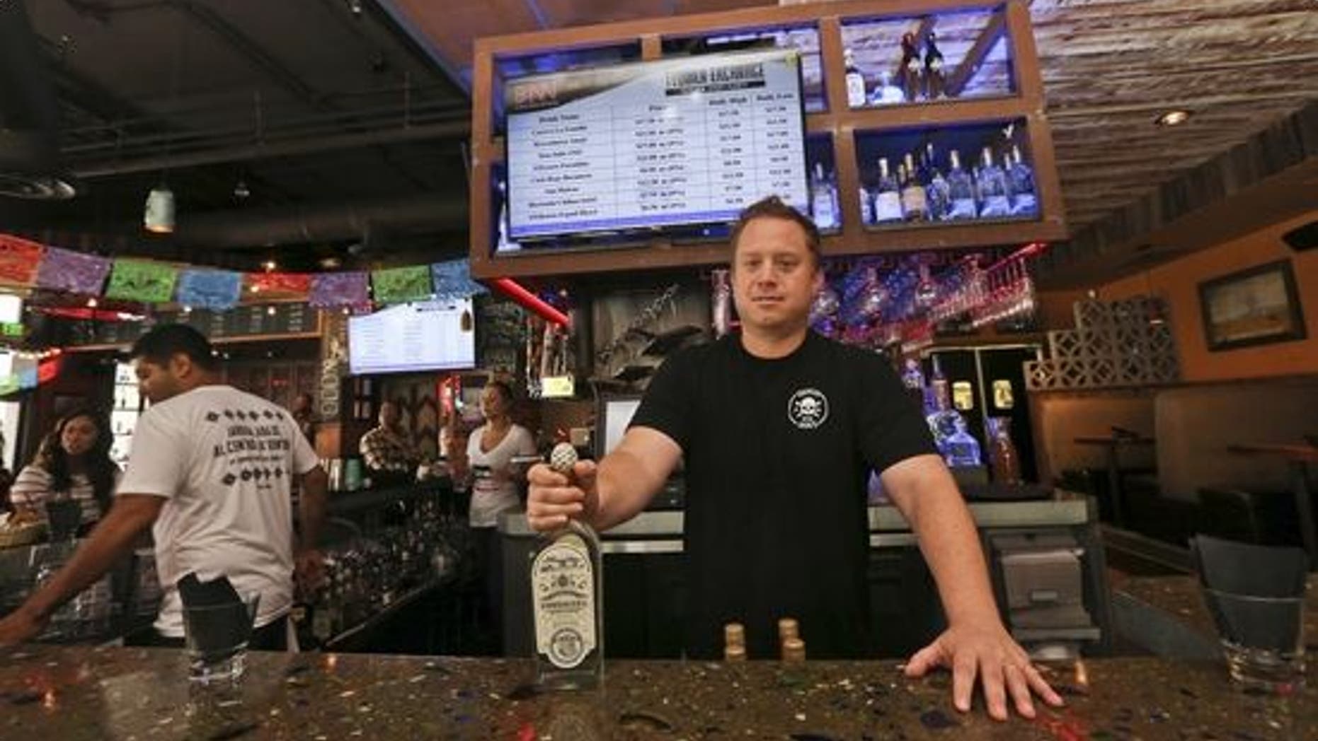 Frank Miller, a partner in a series of eight bars in San Diego, shows off some of the tequila collection at The Blind Burro, in San Diego, where the tequila prices can change every five minutes based on demand. The electronic Tequila Exchange board, behind and above Miller, shows the current prices for the bar's tequila.